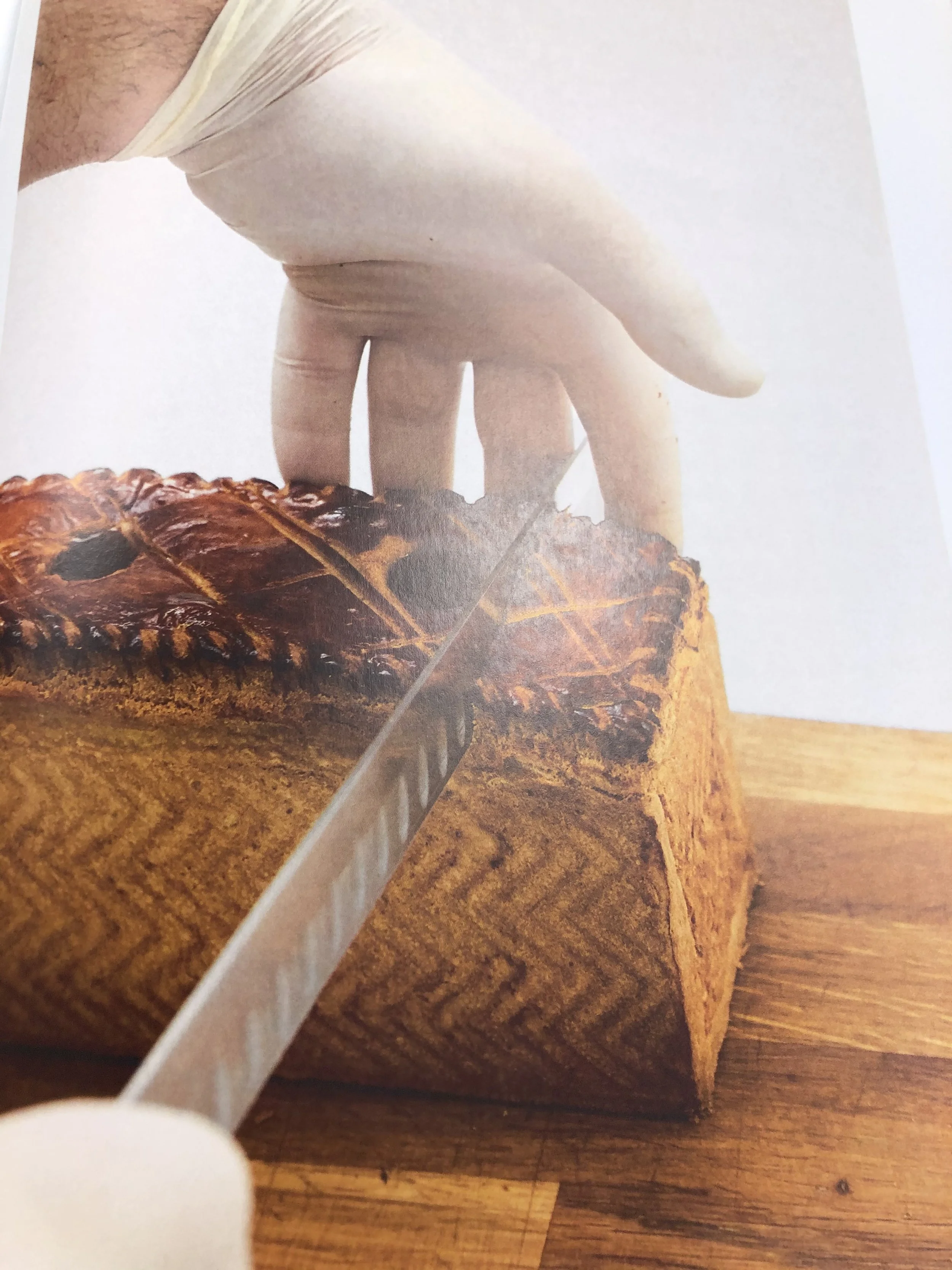 Une main portant un gant blanc coupe un gâteau en bûche de Noël sur une planche en bois.