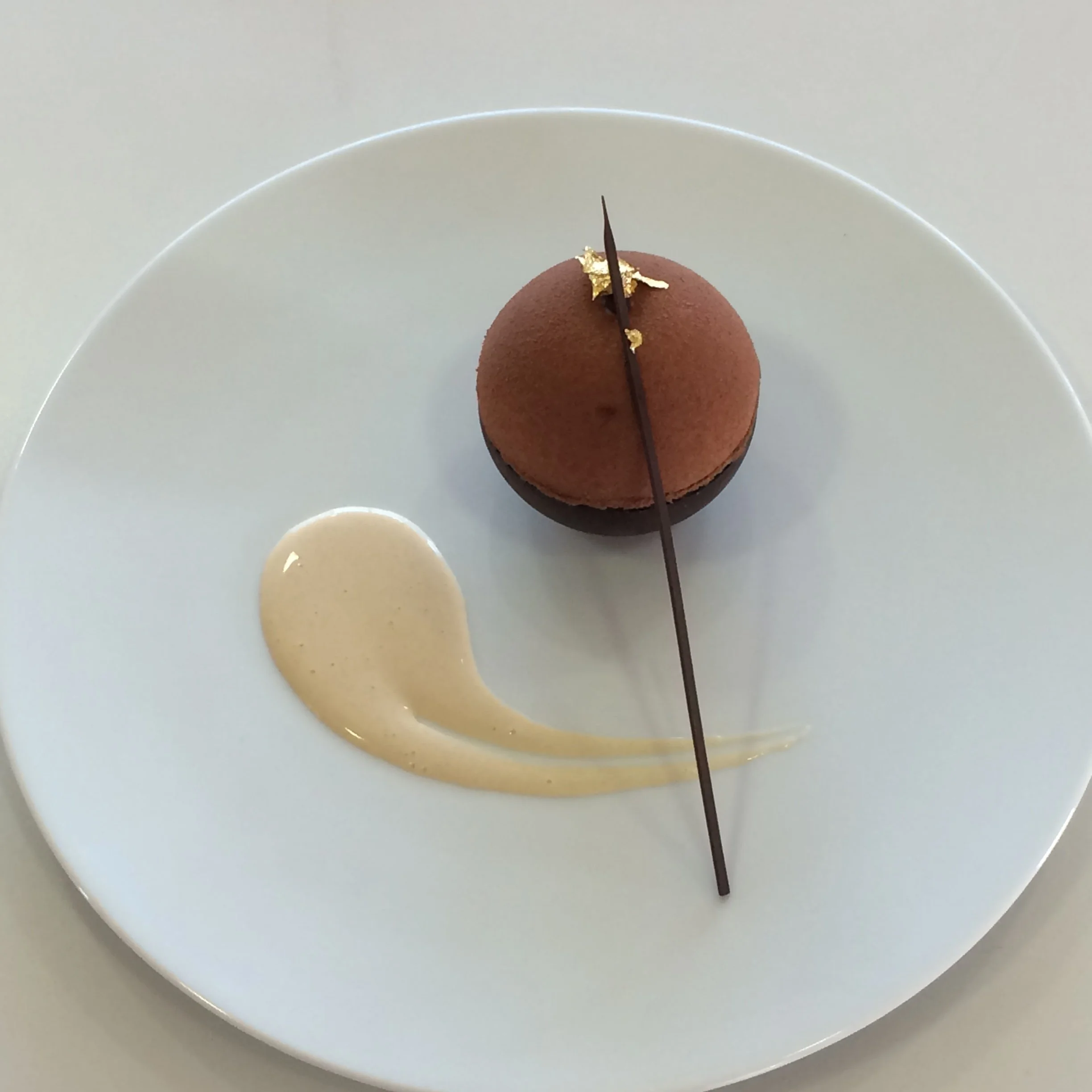 Un dessert chocolaté avec une décoration or et une sauce blanche sur une assiette blanche.