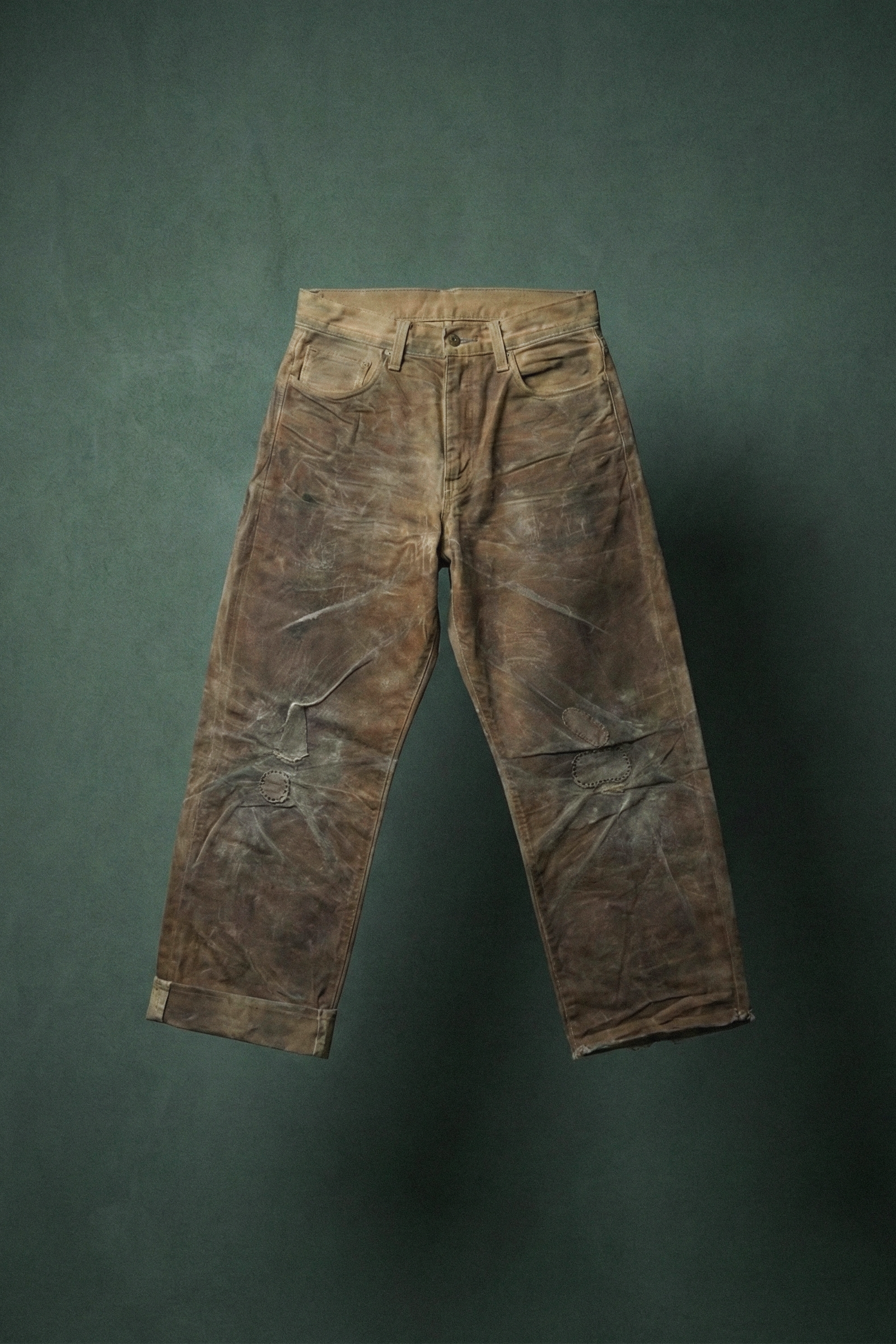 Brown, distressed, and worn-out jeans laid flat on a green surface.
