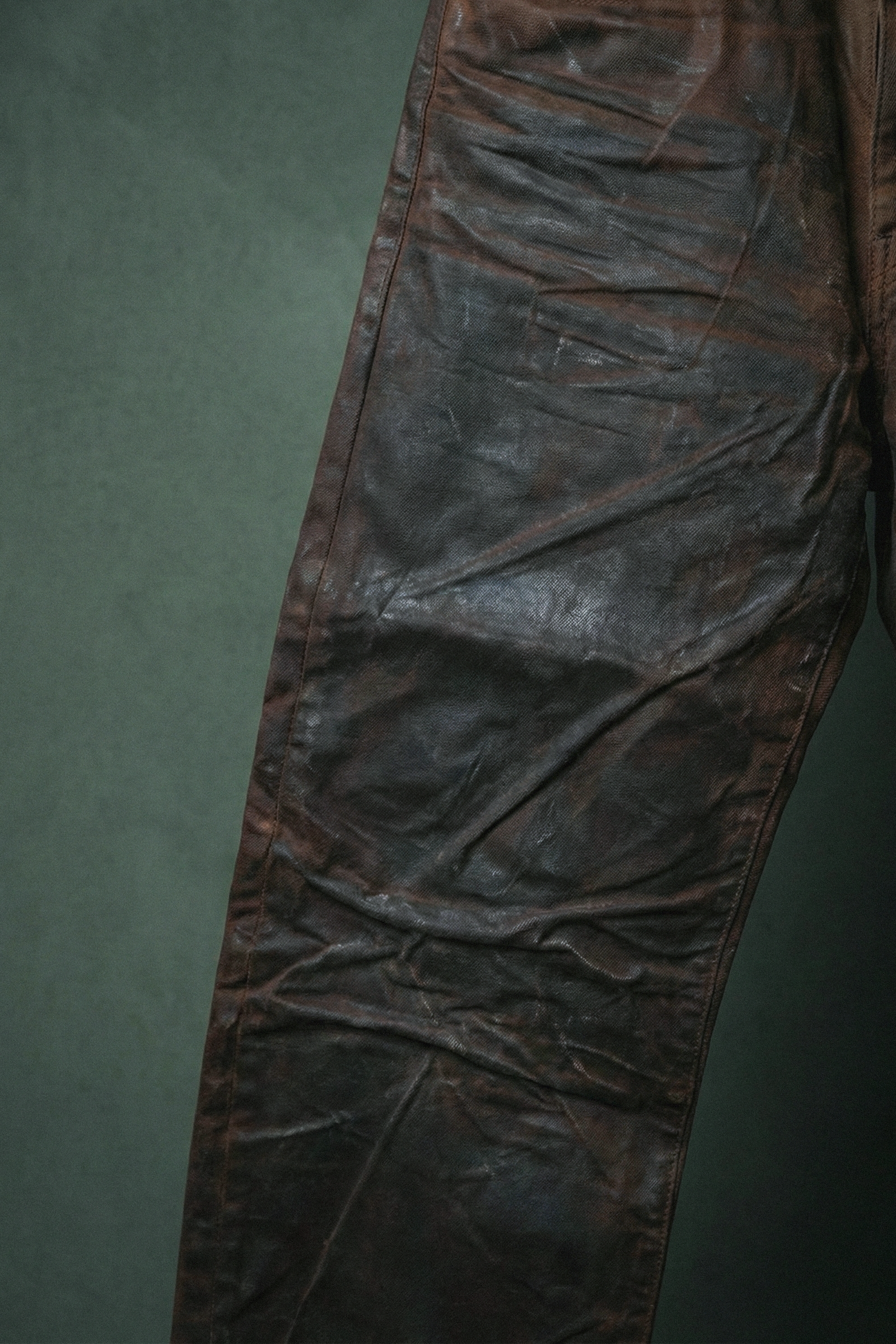 Close-up of a brown leather pant with visible creases and a pocket.