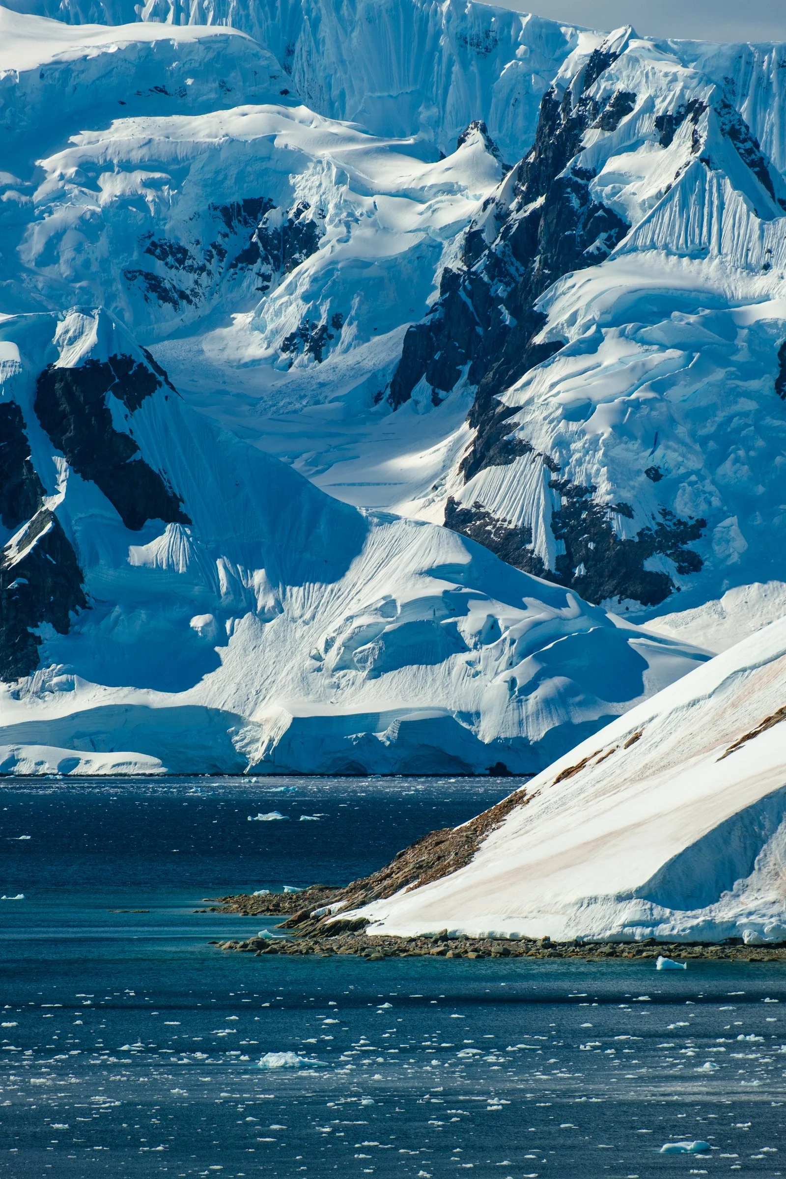 A snowy mountain landscape with glaciers, snow-covered peaks, and an icy water body in the foreground.