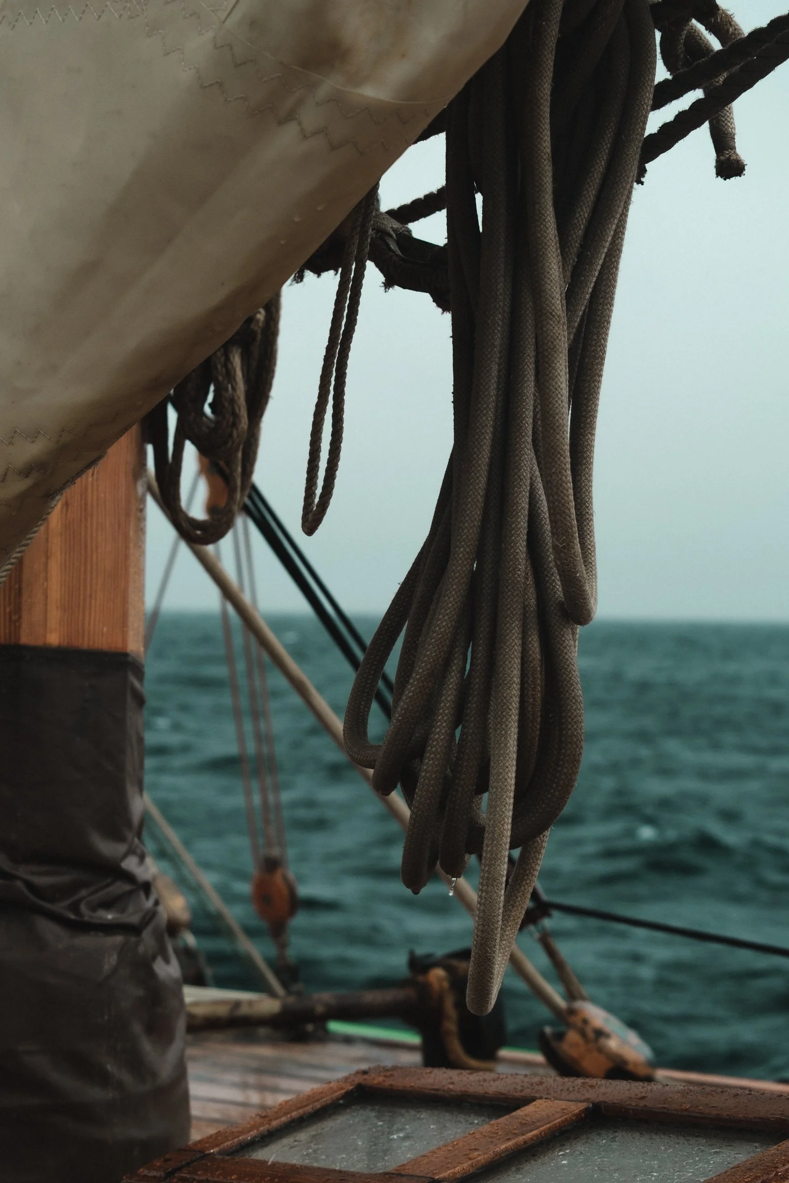 Close-up of ropes and rigging on a sailboat with water in the background.
