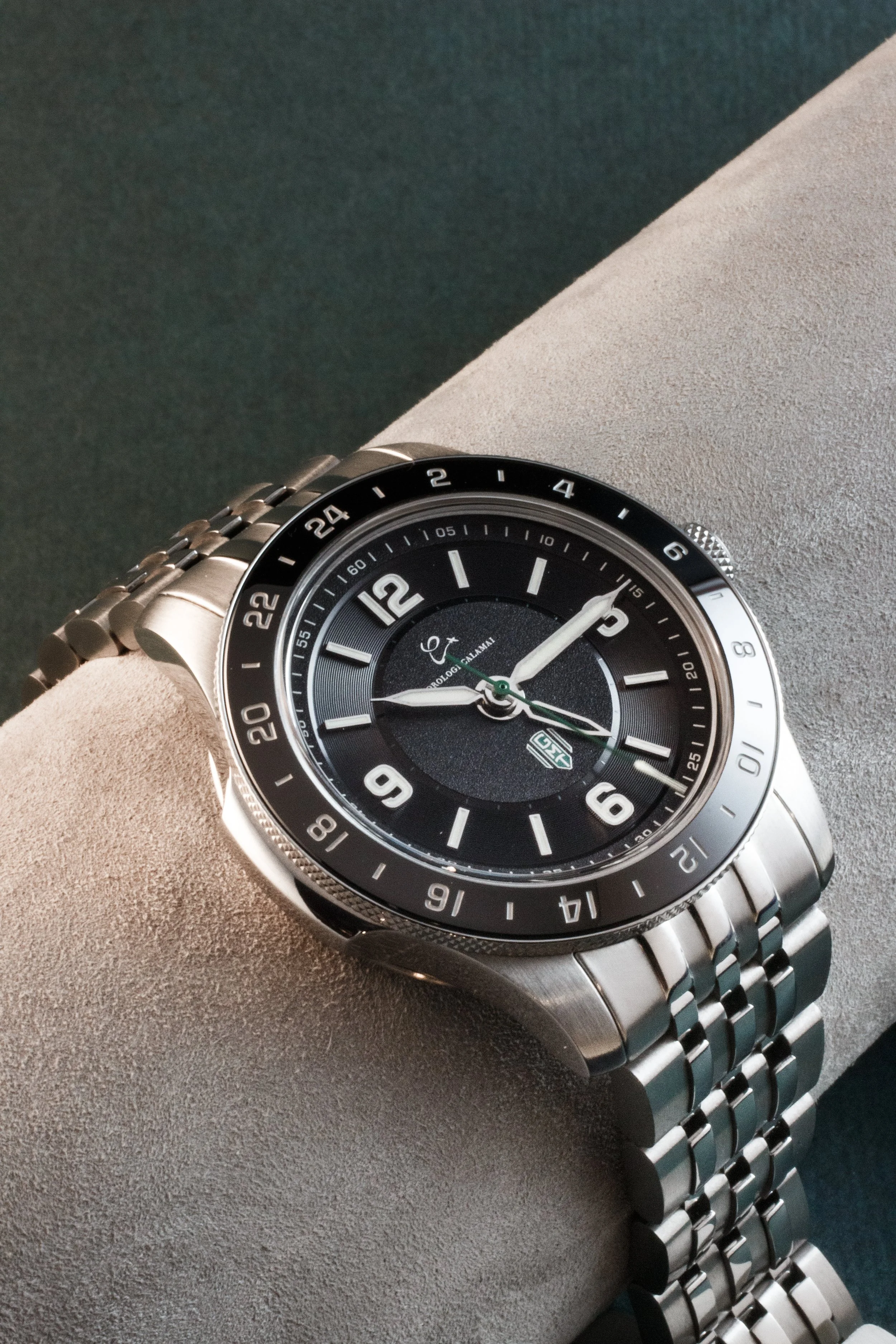 A silver wristwatch with a black dial, displaying time, date, and 24-hour markers, resting on a textured surface.