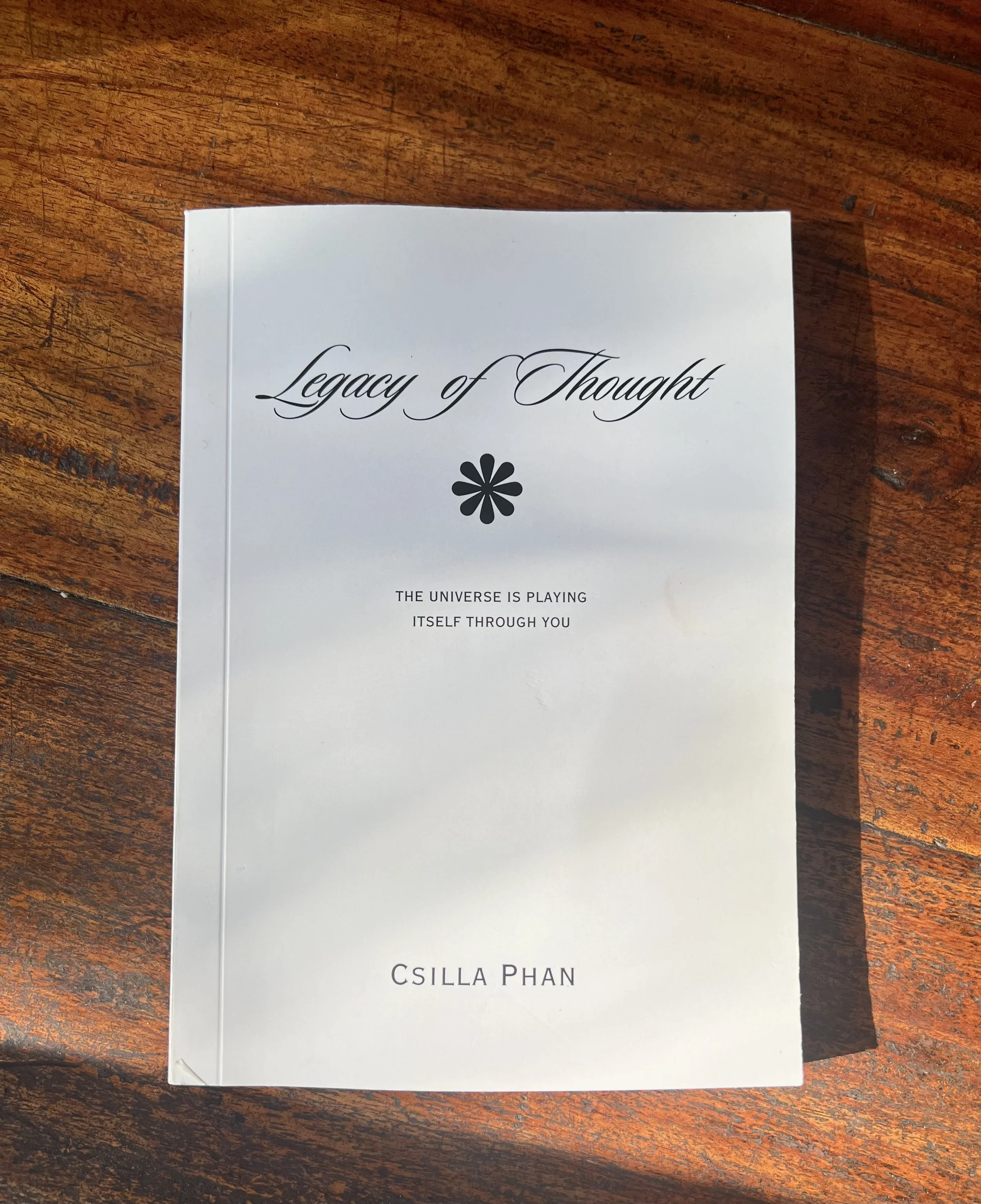 Book titled 'Legacy of Thought' by Csilla Phan resting on a wooden surface.