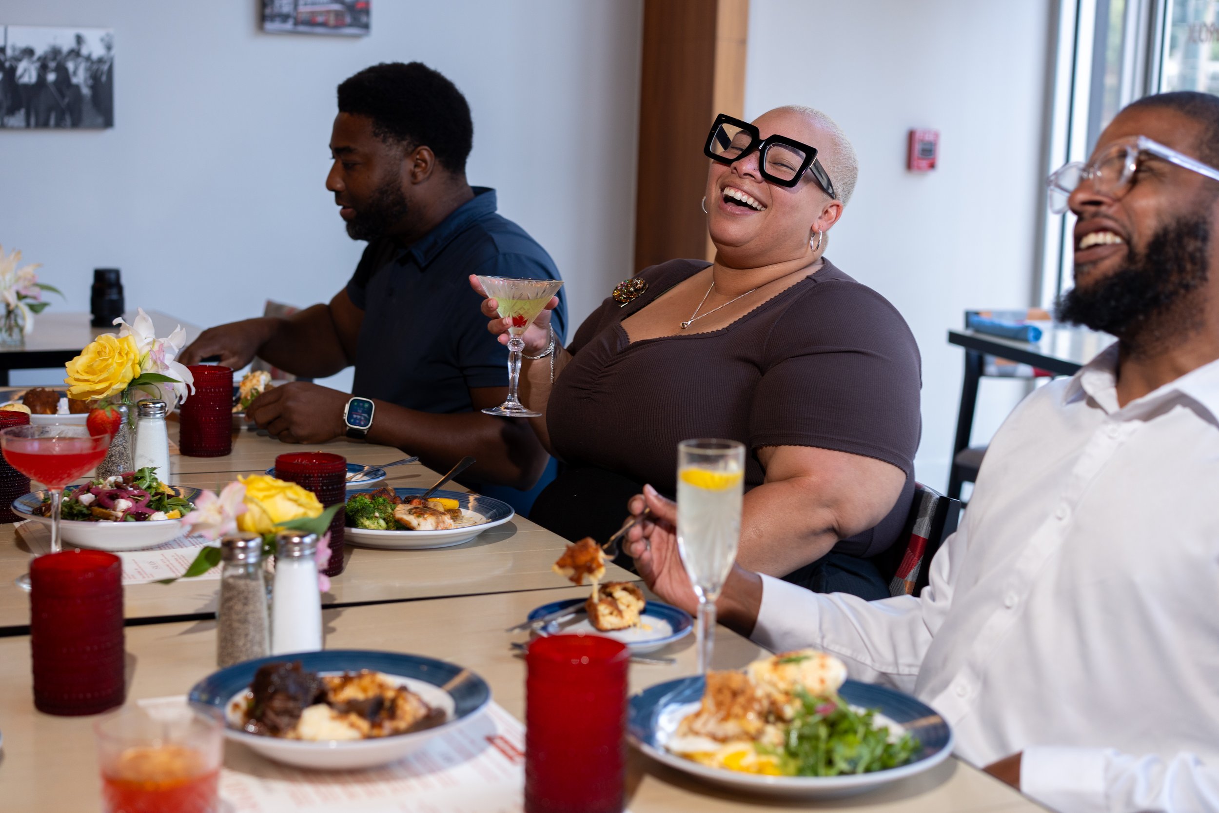 People dining together at a restaurant, laughing and enjoying a meal, with food and drinks on the table.