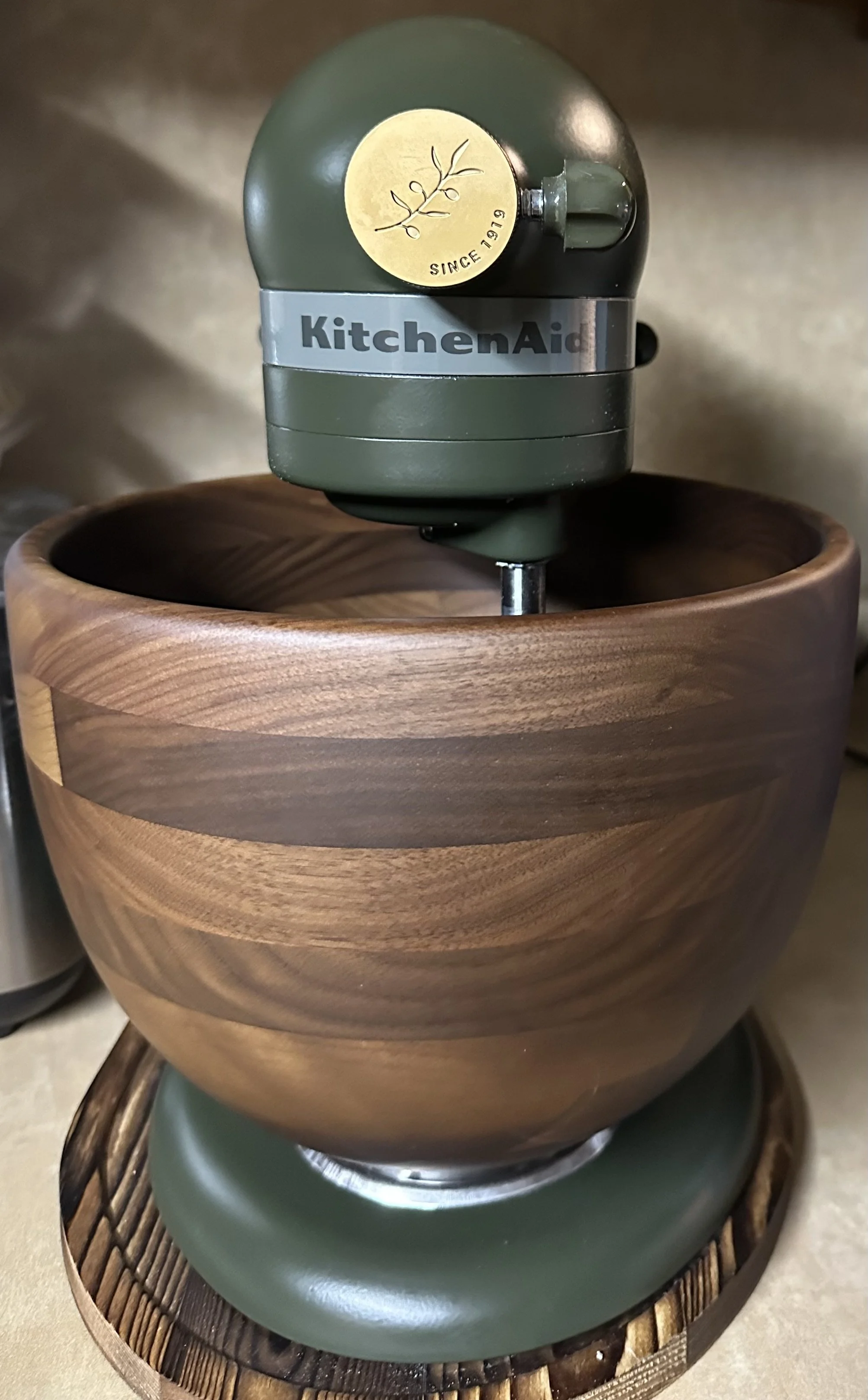 A KitchenAid stand mixer with a wooden bowl, placed on a wooden base.