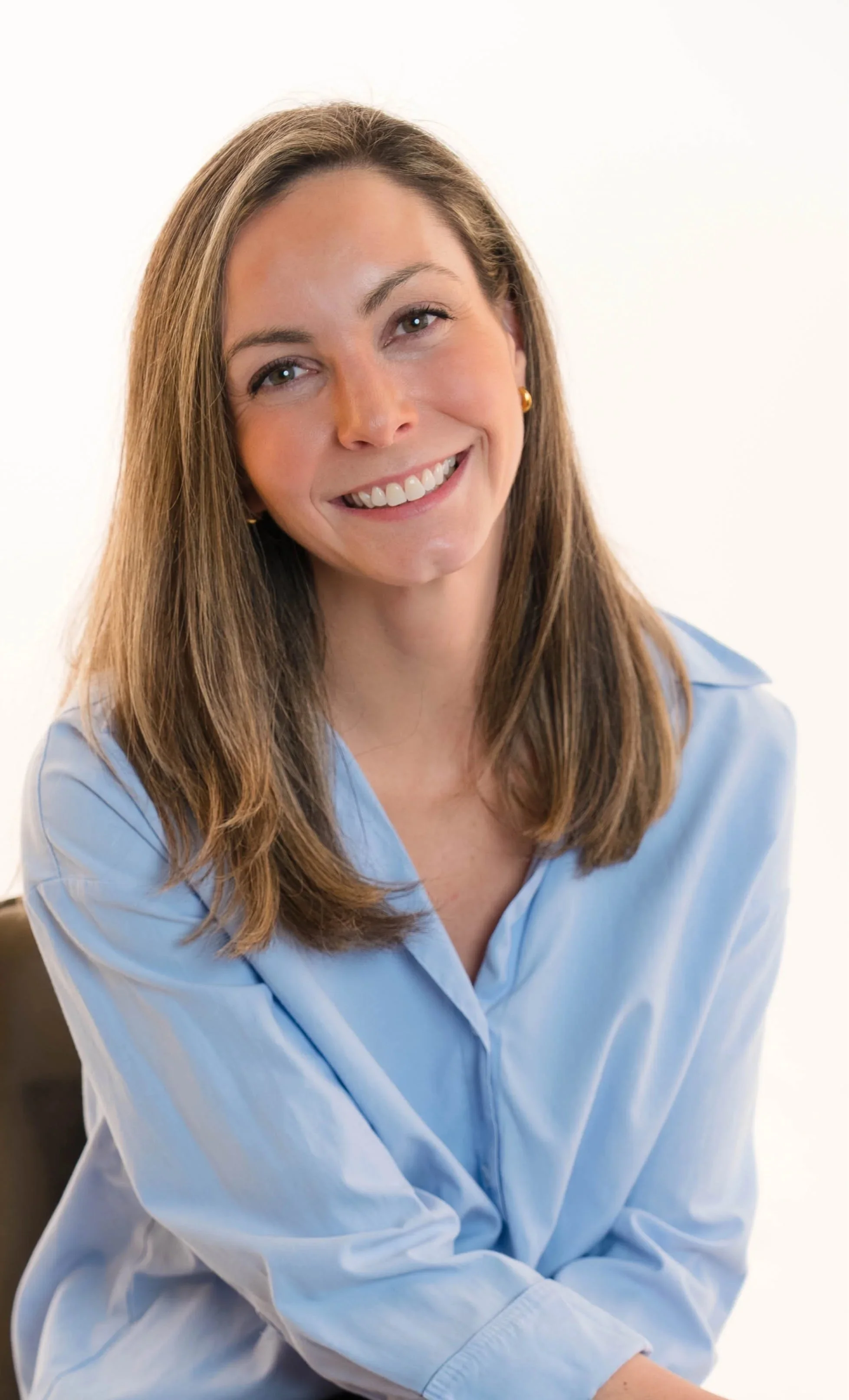 A smiling woman with shoulder-length brown hair, wearing a light blue blouse, posing against a plain white background.