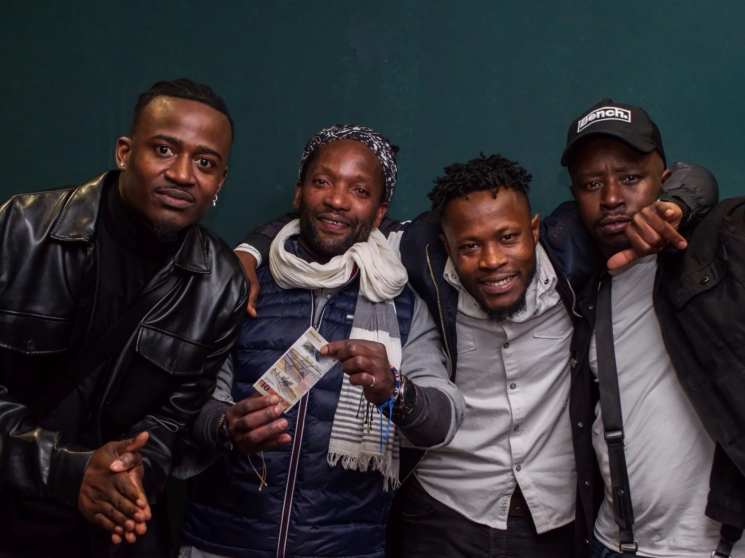 A group of five men indoors, sitting close together, smiling, and posing for a photo. One man in the center is holding a 10 Euro banknote. Event photography in Letterkenny, Derry, Belfast, afro night. 