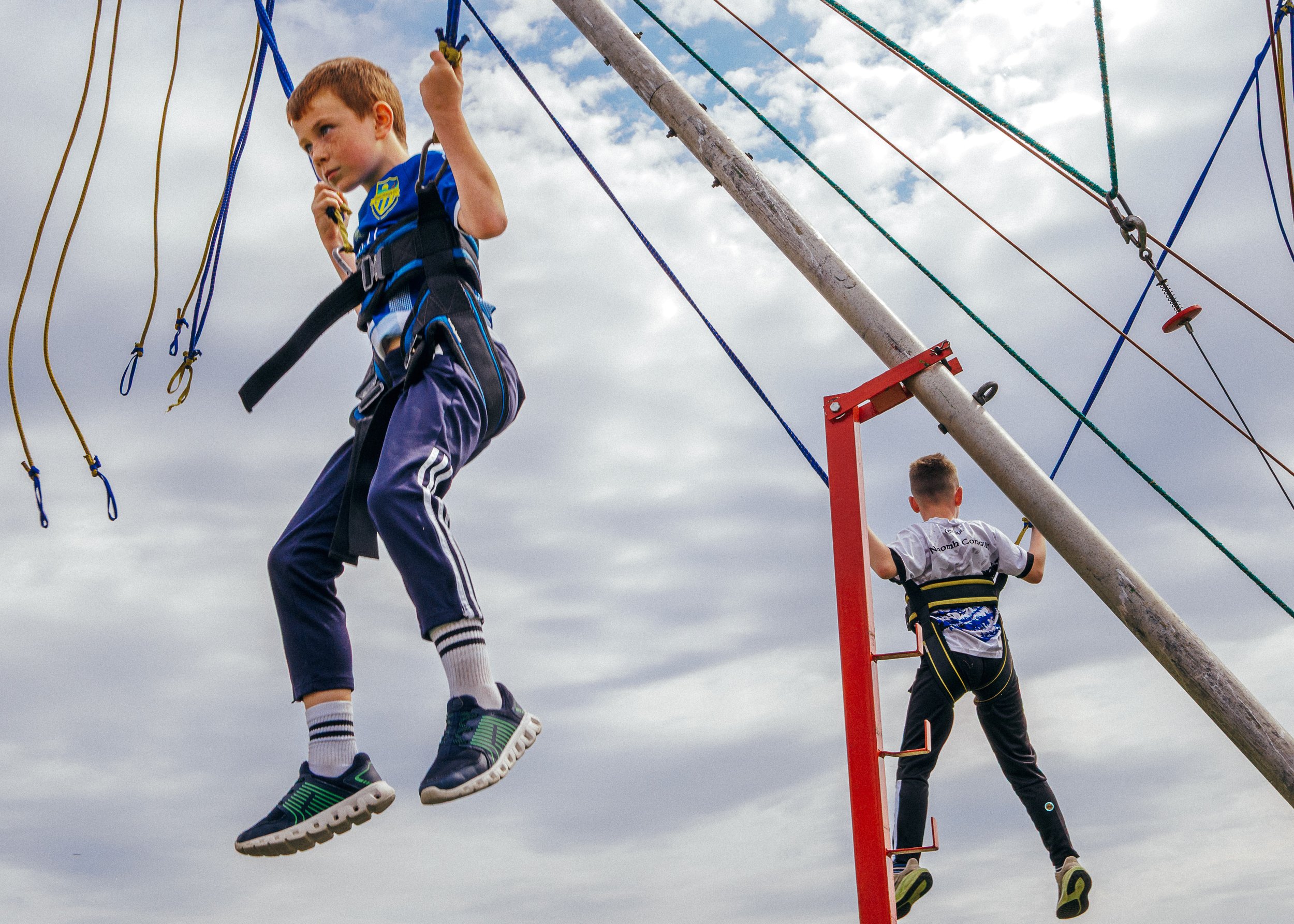 Children climbing a rope net ladder on a playground against a cloudy sky. Clonmany agricultural show. Donegal. Kids entertainment. Donegal Fair. 