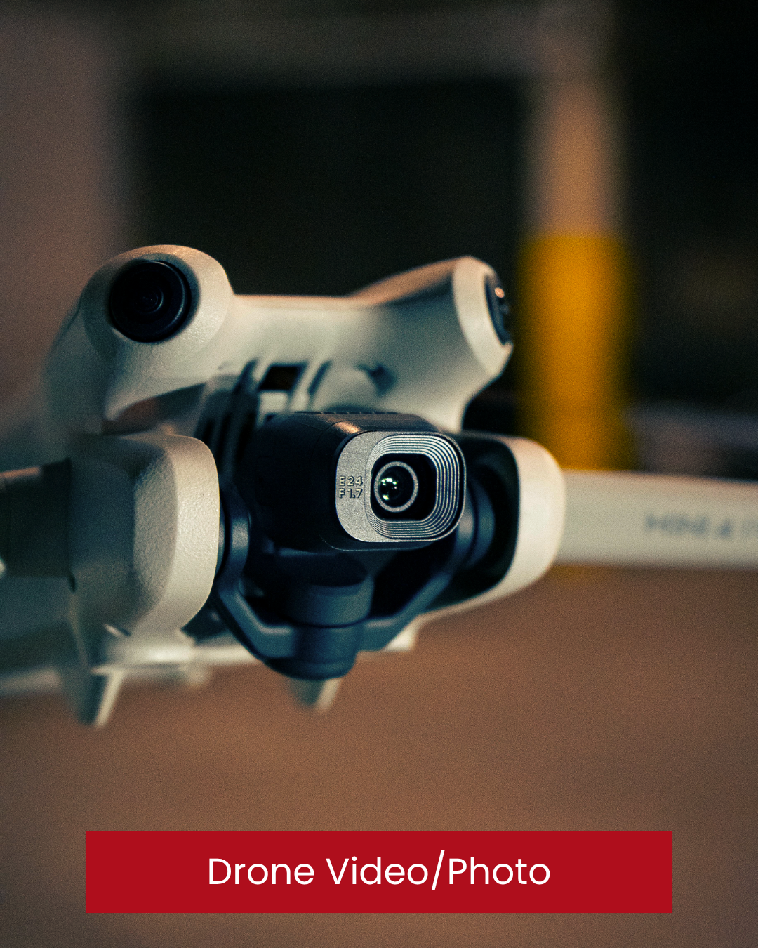 Close-up of a drone camera mounted on a white quadcopter drone, with a blurred background and a red label at the bottom reading "Drone Video/Photo." Drone specialist. Drone videography in Donegal. Real estate.