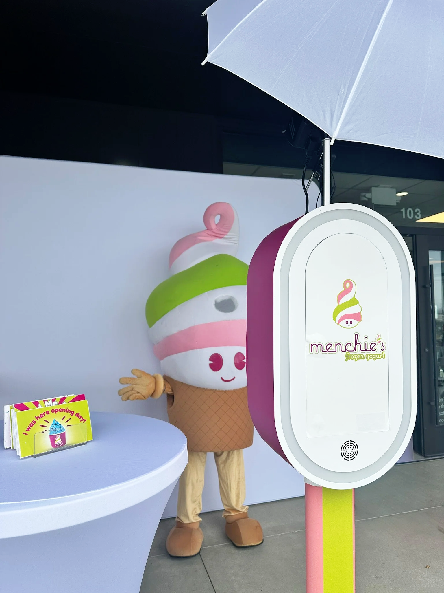 A mascot dressed in a large ice cream cone costume standing next to a Menchie's frozen yogurt in Everett Washington for their grand opening, fully branded photo booth.