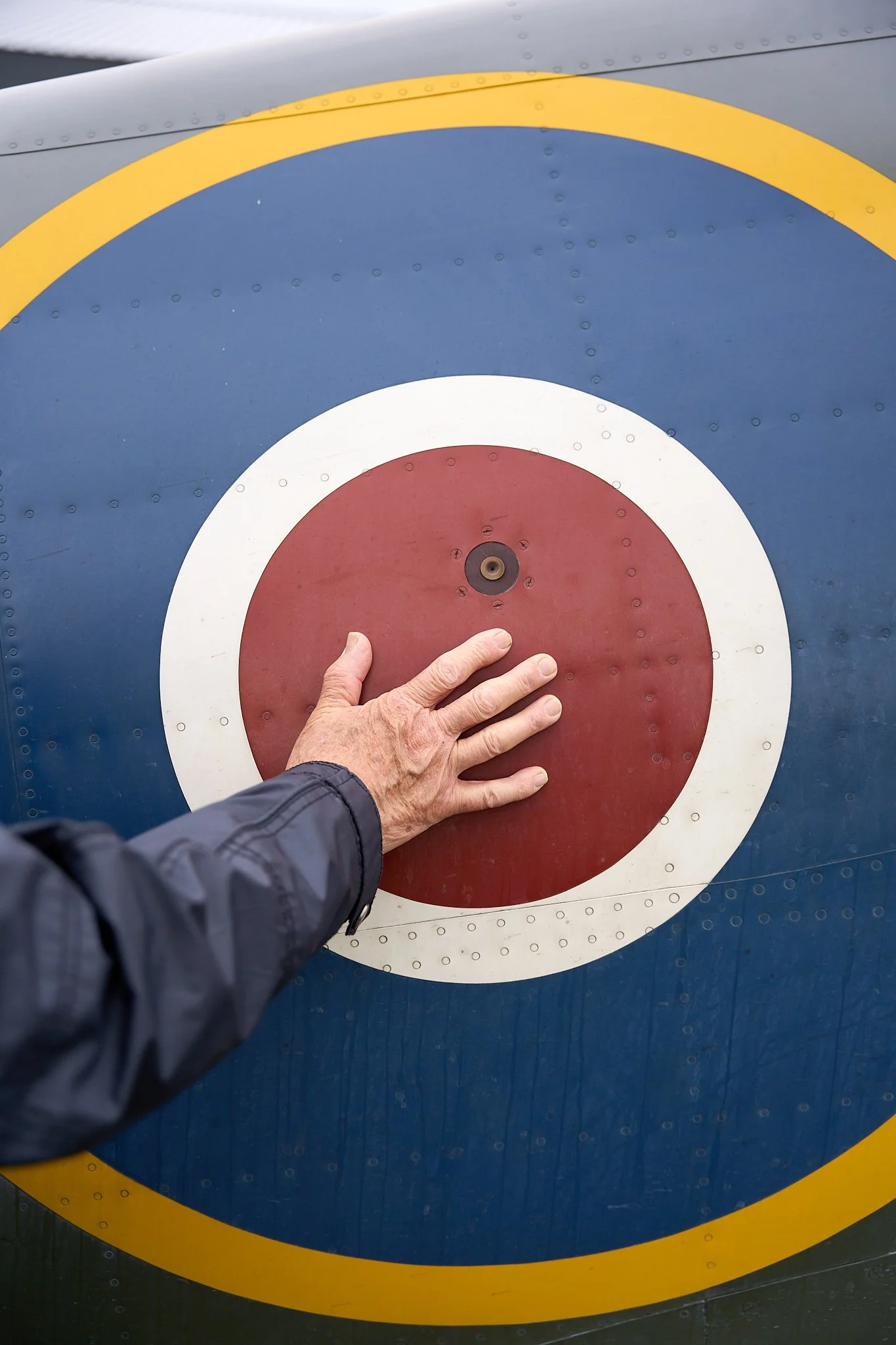 A person's hand is touching the center of a red and white target painted on a blue surface, likely part of an aircraft.