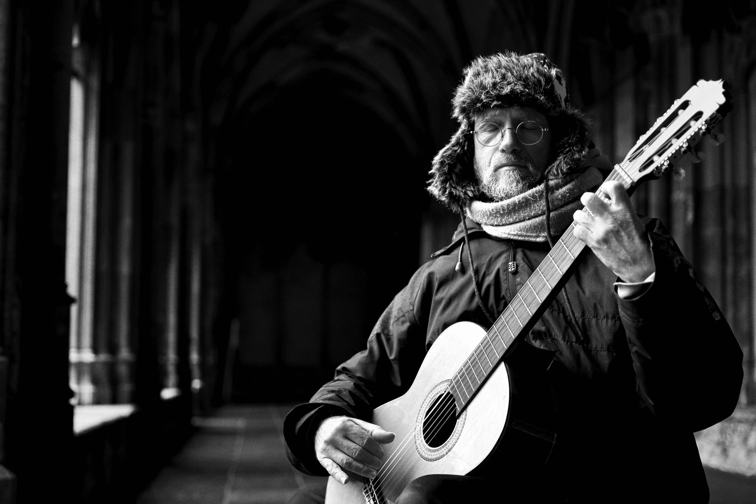 Man in een donsjas en alpaca hoed speelt gitaar in een donkere gang