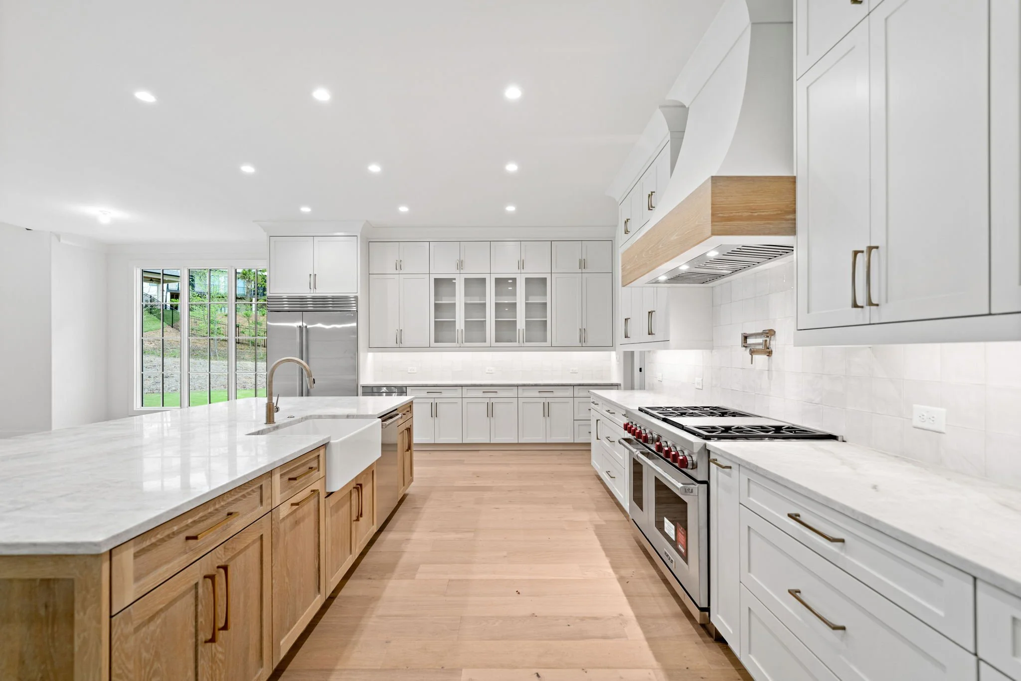 Modern kitchen with white and wooden cabinetry, stainless steel appliances, and a large island with bar seating. Bright and spacious with natural light from windows.