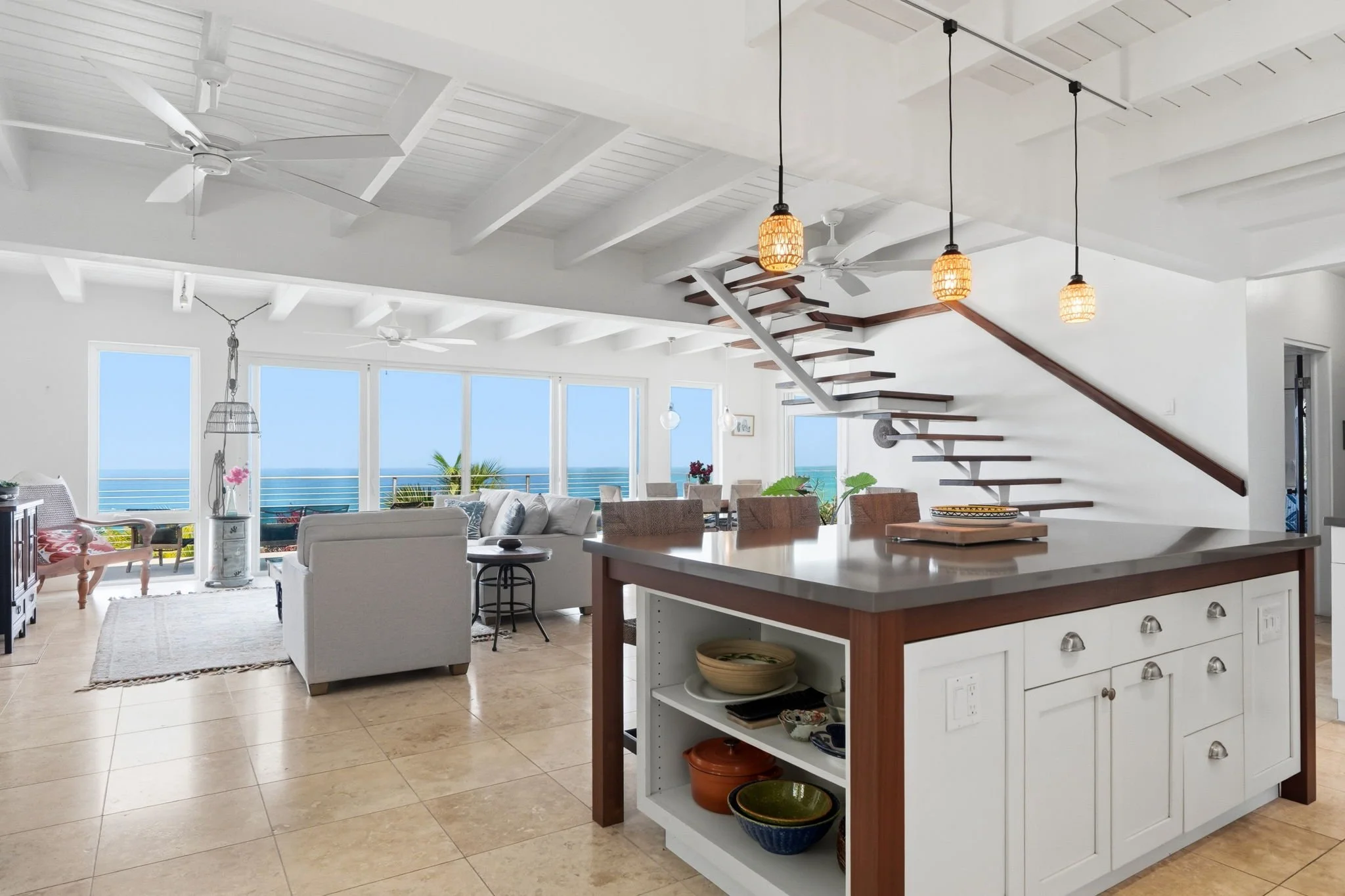 Modern kitchen with light wood cabinets, black appliances, a kitchen island, pendant lights, a window view of trees, and a herringbone backsplash.