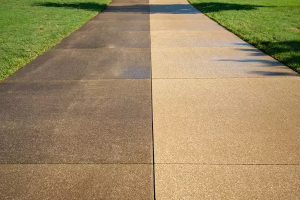 A sidewalk with two different colored concrete sections, one darker and one lighter, bordered by green grass on both sides.