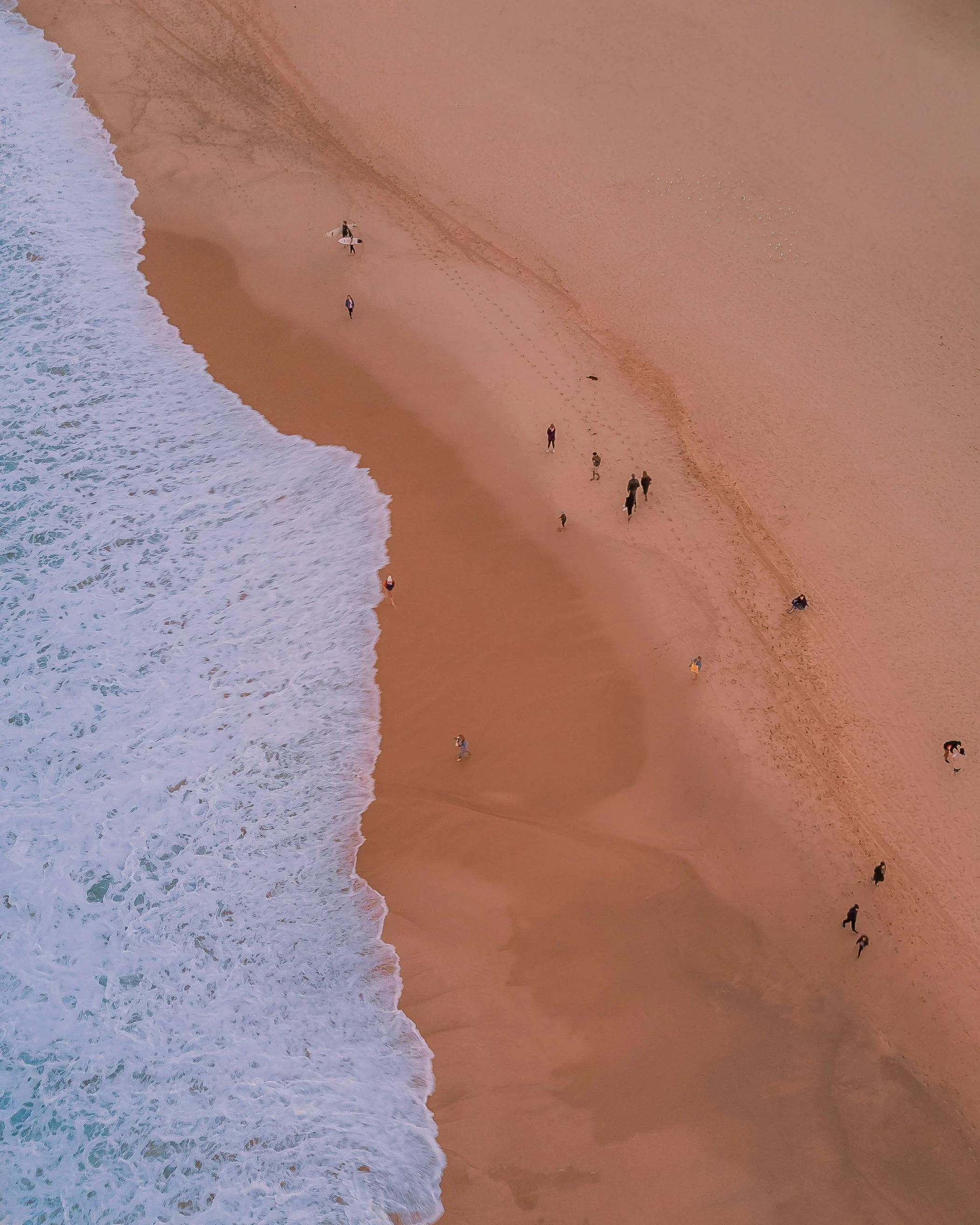 overview shot of a coastline, pink sand, people walking, ocean wake showing