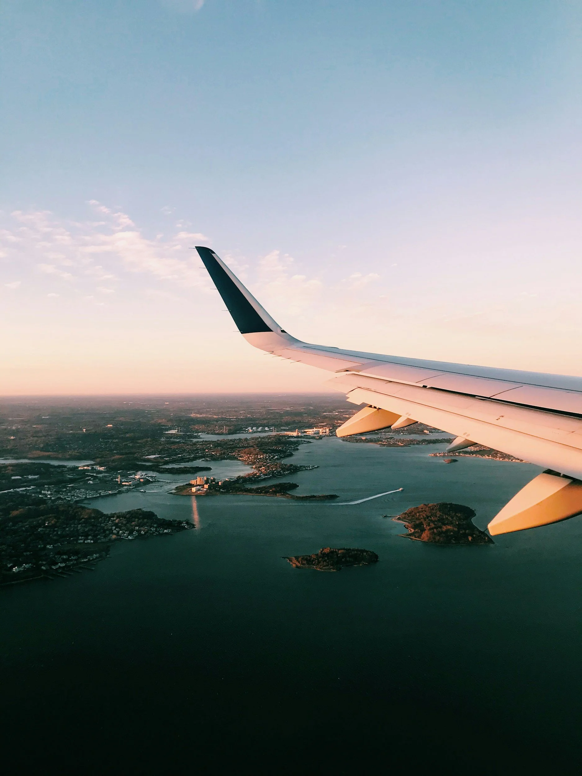 View of the airplane wing and landscape below from an airplane window during sunset.