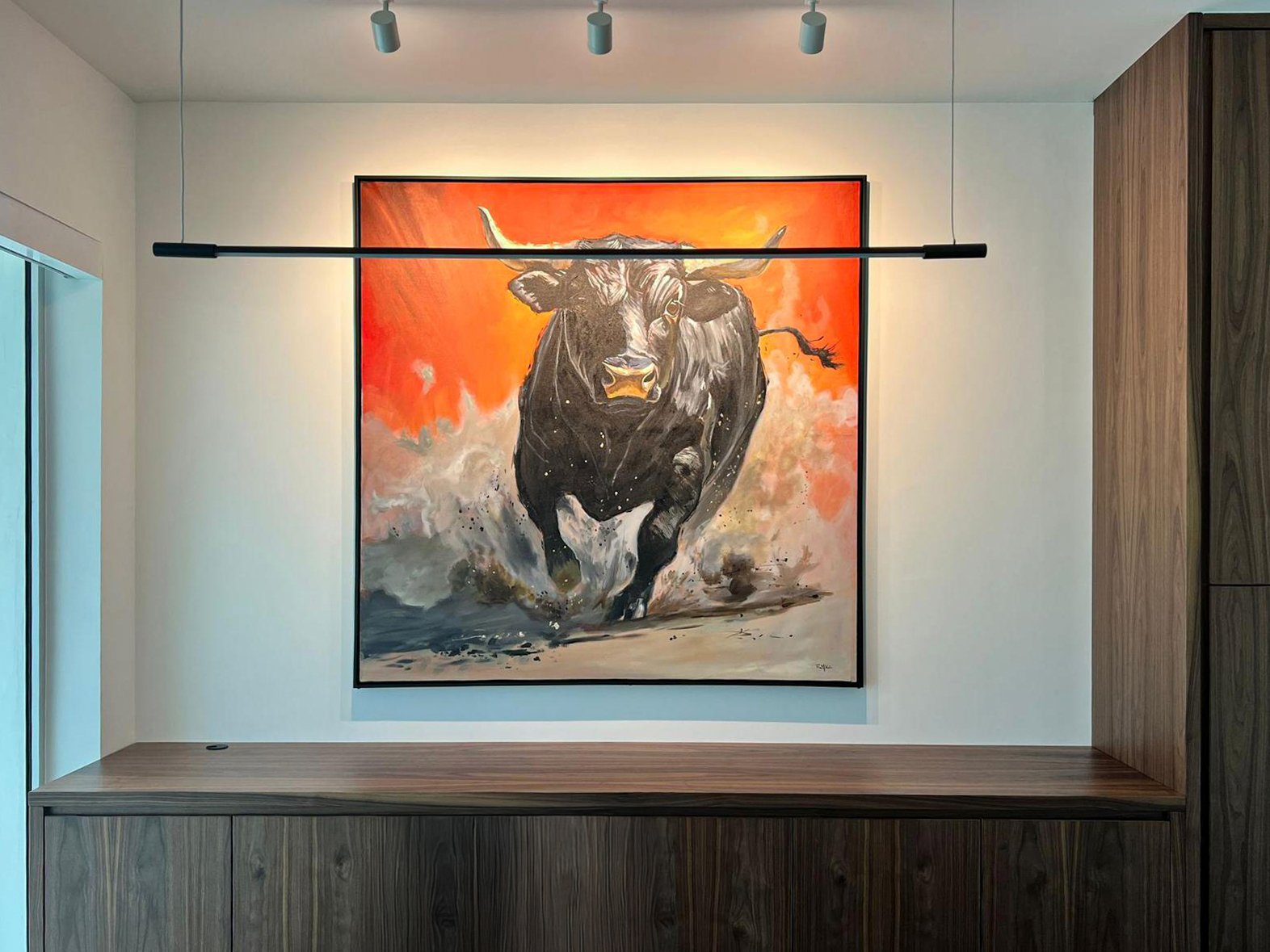 Painting of a black bull charging with an orange background, displayed on a white wall in a modern interior.