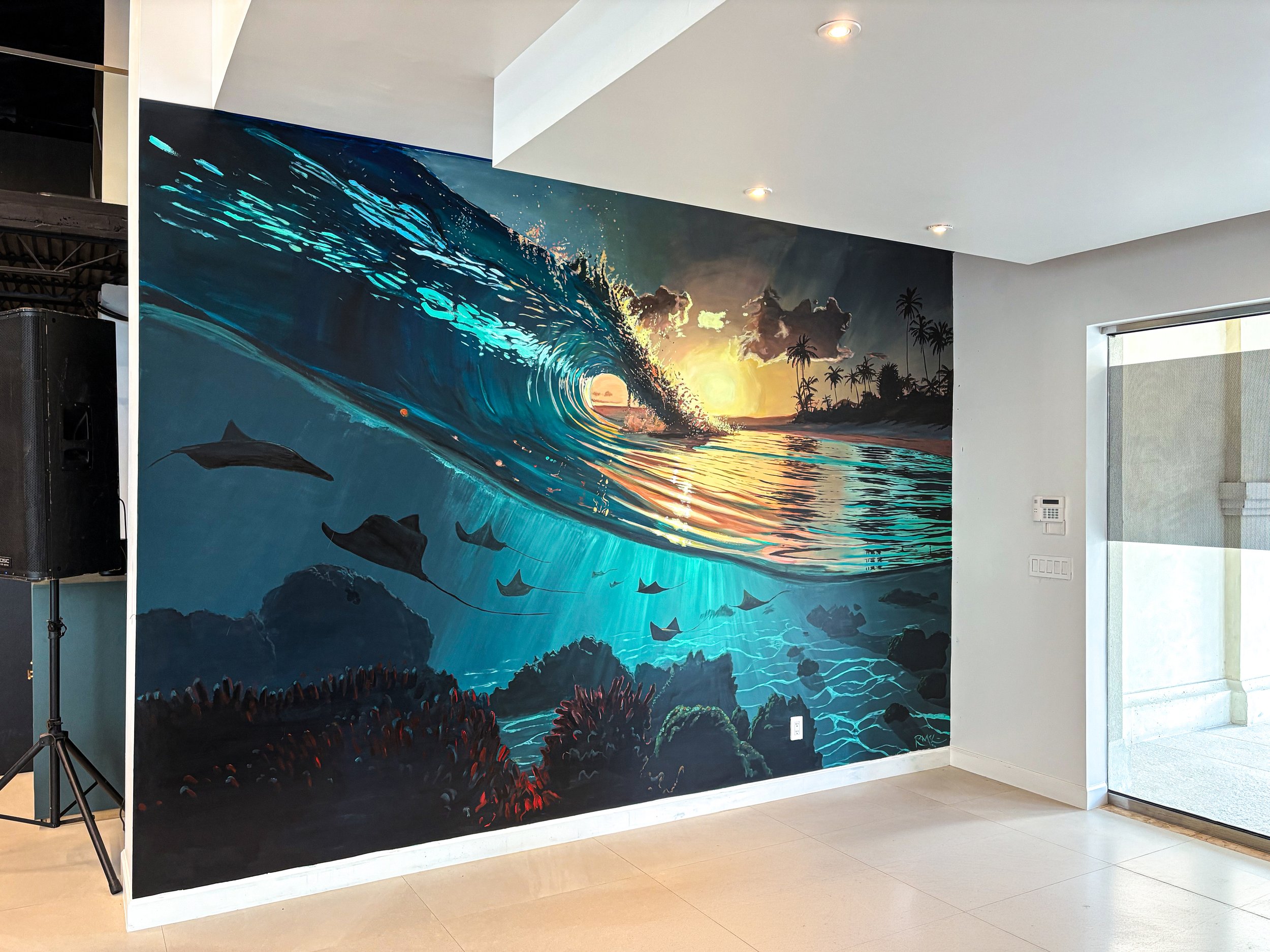 Mural of an ocean scene with a large wave, dolphins, coral reef, and sunset with a tropical island and palm trees