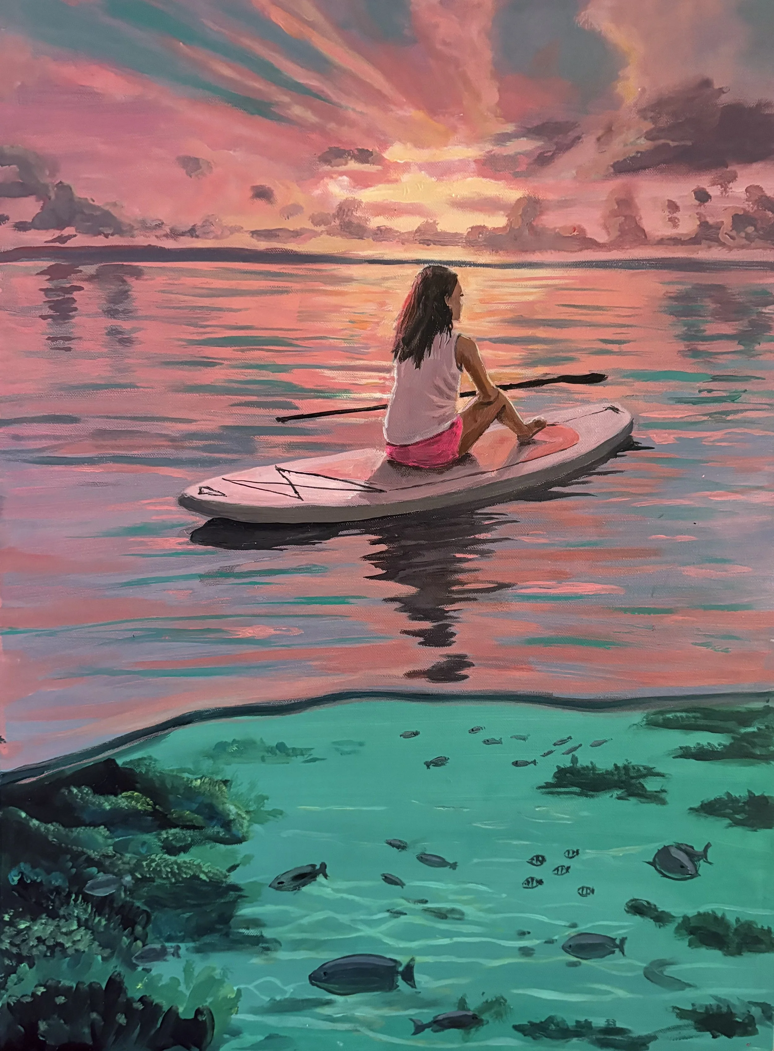 A girl sitting on a paddleboard on a calm body of water during sunset, with fish swimming below and a colorful pink sky with clouds overhead.