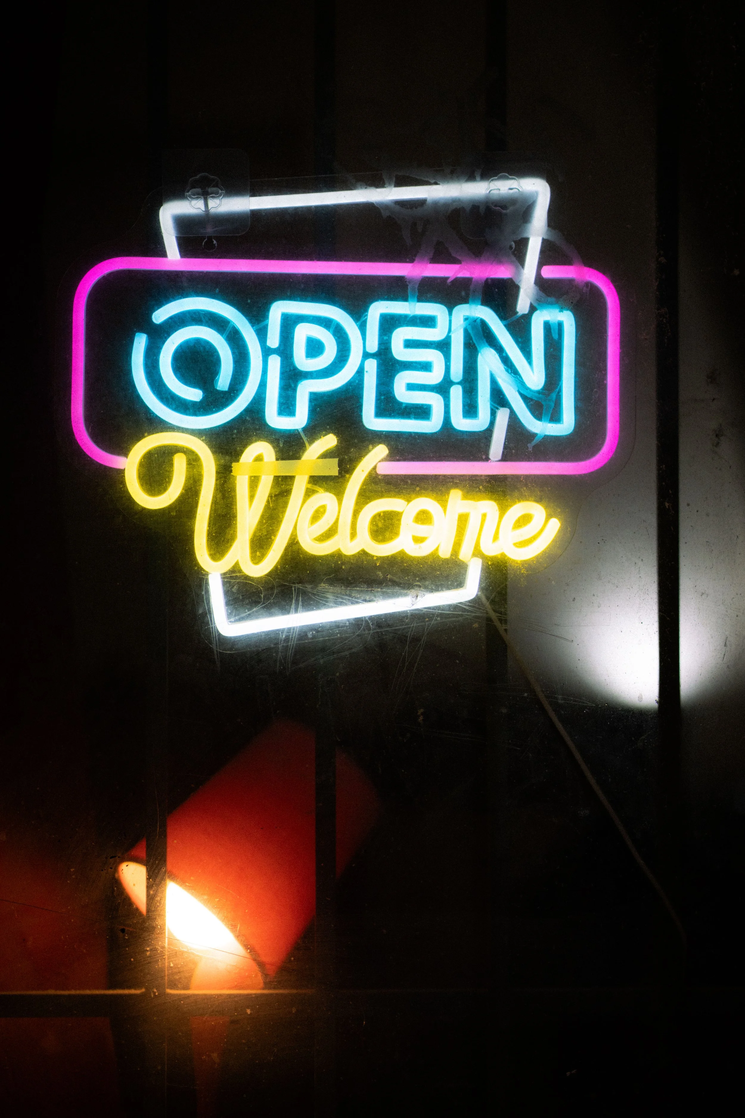 enseigne lumineuse colorée affichant "OPEN" en bleu, "Welcome" en jaune, avec un fond sombre.