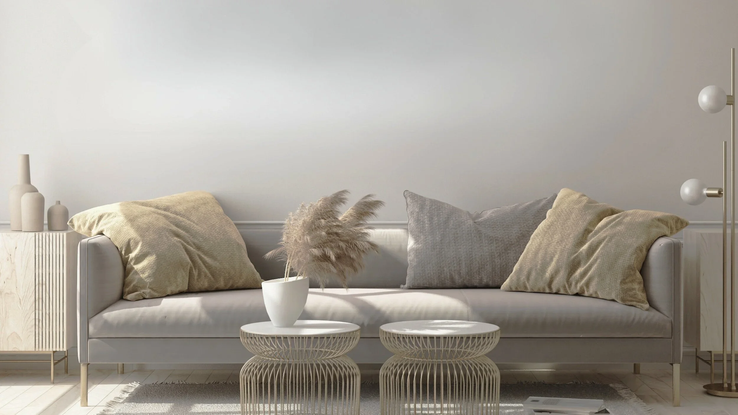 A minimalist living room with a white sofa, beige and gray cushions, a white vase with pampas grass on matching round tables, a sideboard with vases, and a modern floor lamp, all in neutral tones.