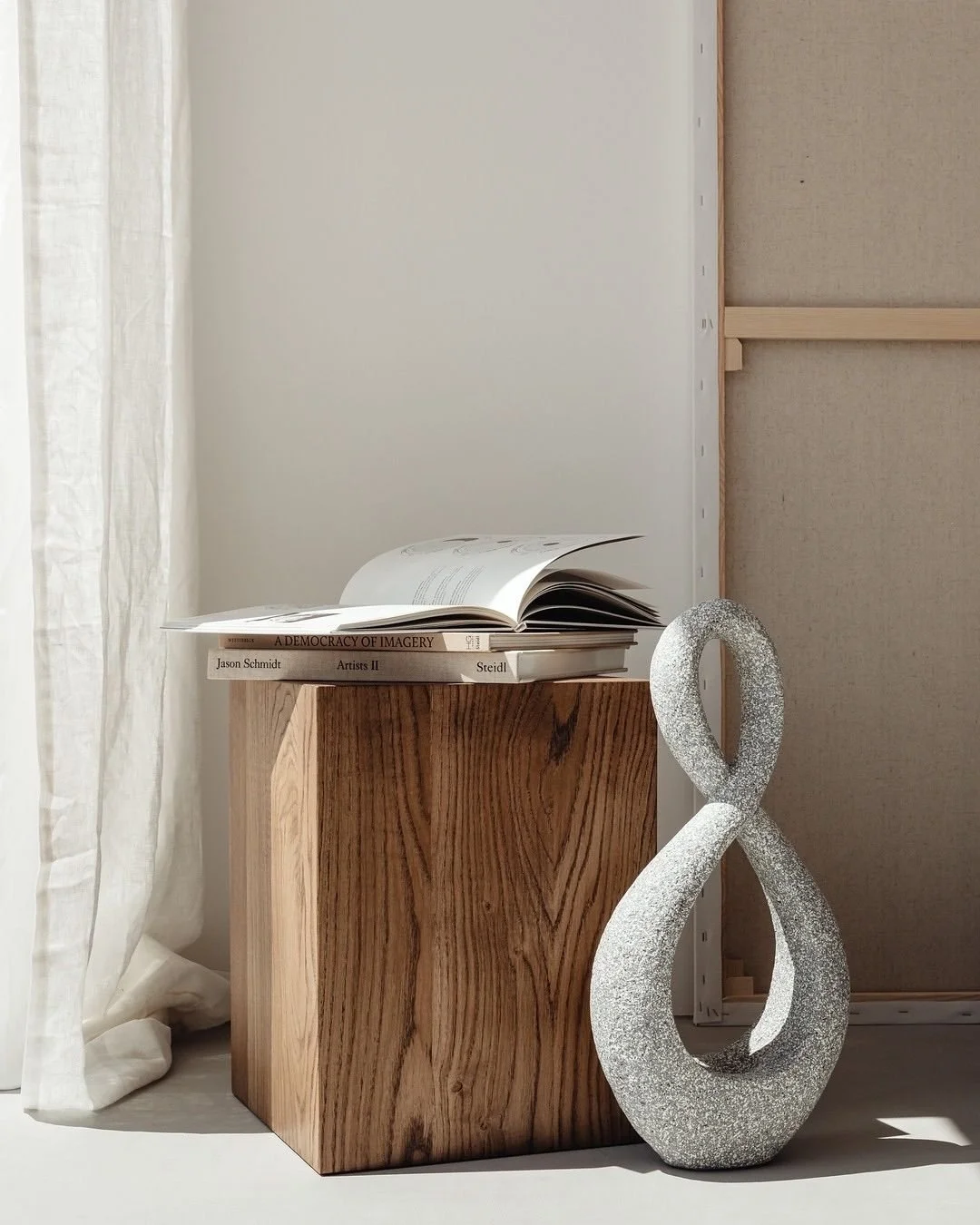 Stack of three art books on wooden block with sculpture beside and white curtains on the side.