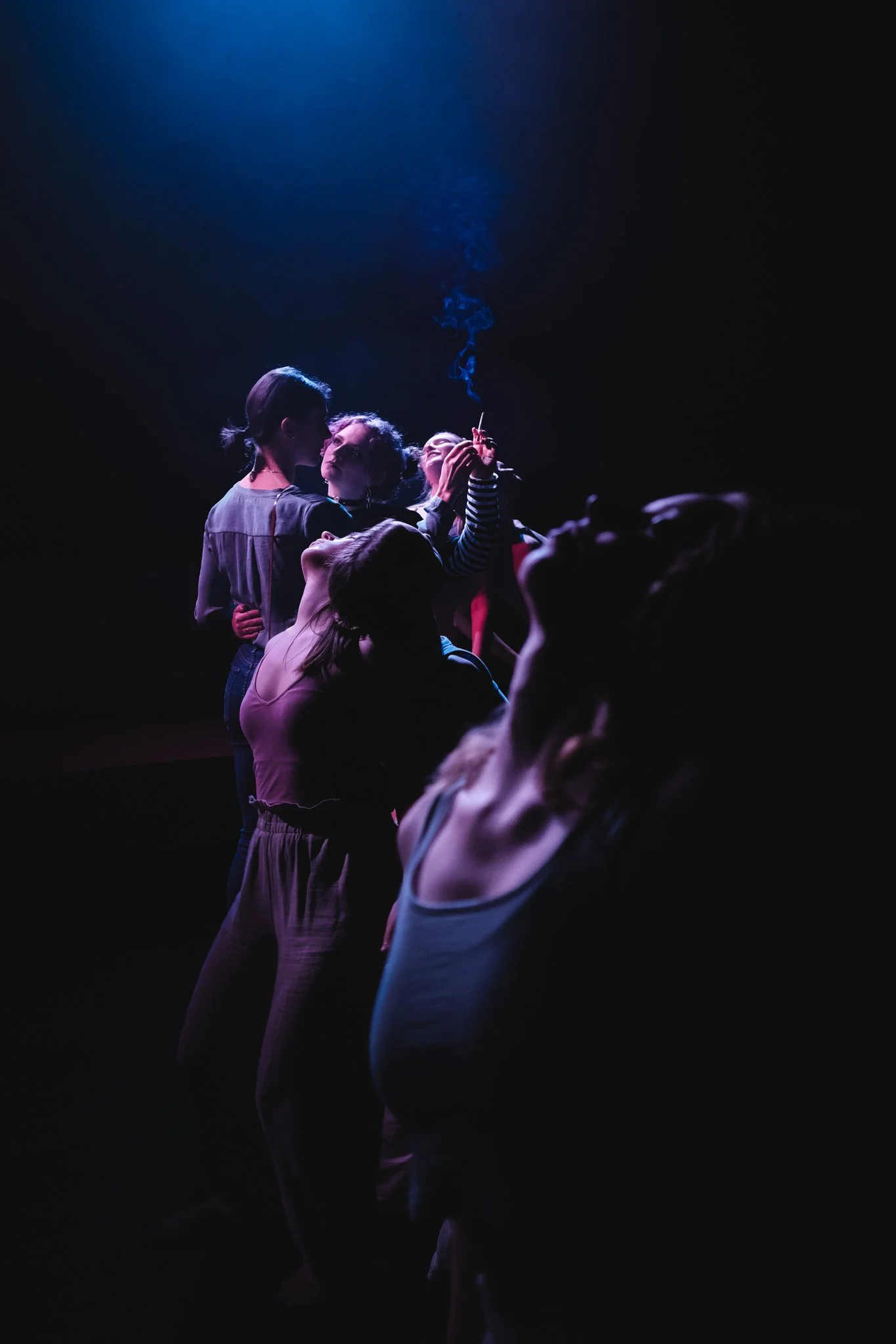 Gruppe aneinander lehnender Personen im Schatten bei einer Party, hinten zwei Frauen im Fokus erhellt, eine Zigarette glimmt zwischen den Händen der beiden Frauen.