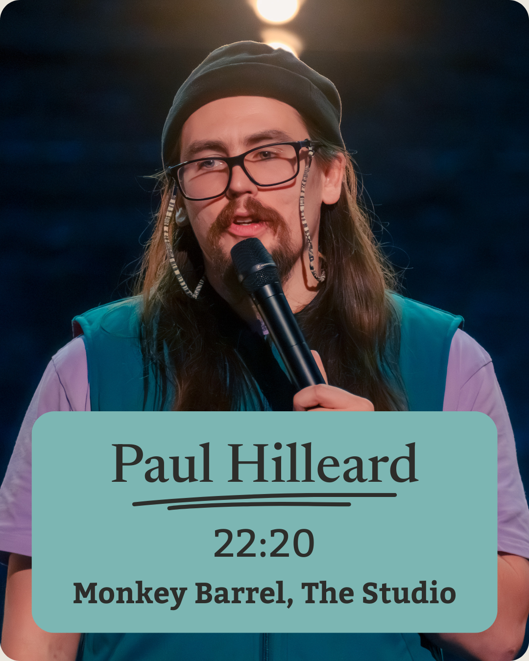 A man with long hair, glasses, and a beard, holding a microphone and speaking, standing in front of a dark background with bright lights overhead. The image has a text overlay that reads "Paul Hilleard," with a showtime of "22:20," and mentioning the