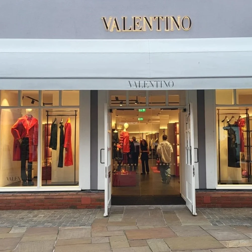 Valentino clothing store entrance with mannequins dressed in red and black outfits displayed in the windows