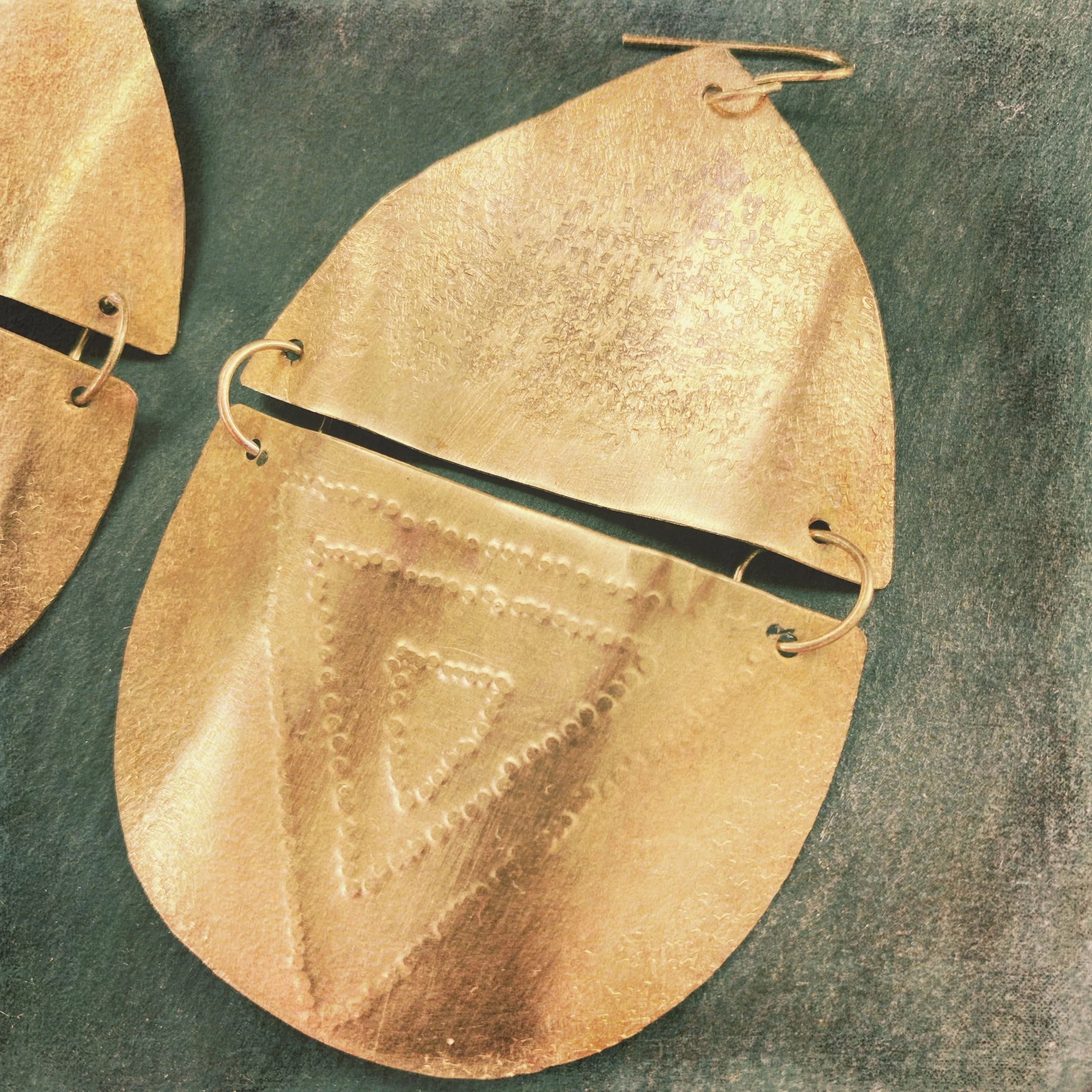 Close-up of gold-colored metallic sand dollar-shaped jewelry with etched designs, placed on a dark surface.