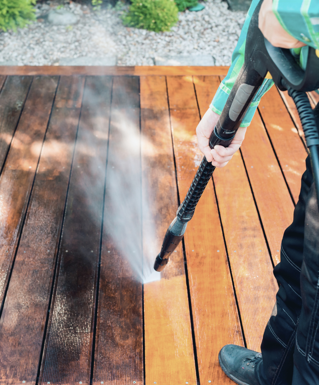 Person pressure washing a wooden deck outdoors.