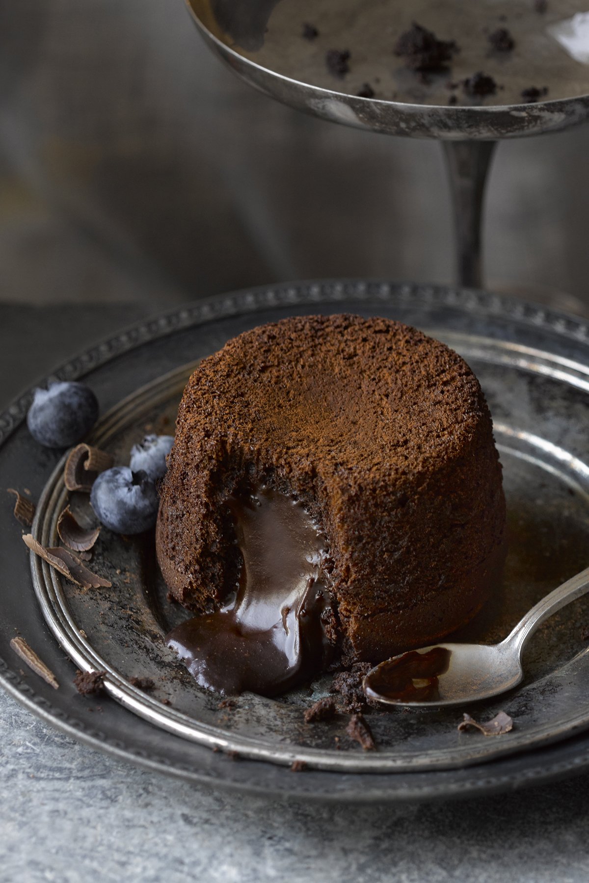 Chocolate lava cake with a spoonful pouring out melted chocolate, garnished with blueberries and chocolate shavings.
