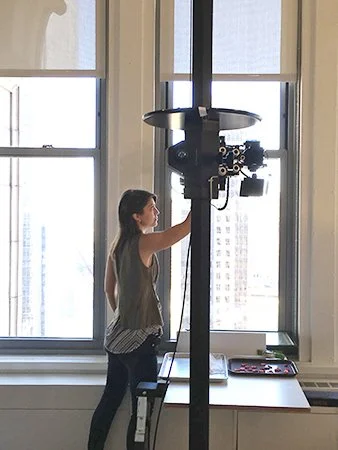Woman operating film or digital camera mounted on a tall stand in front of large windows