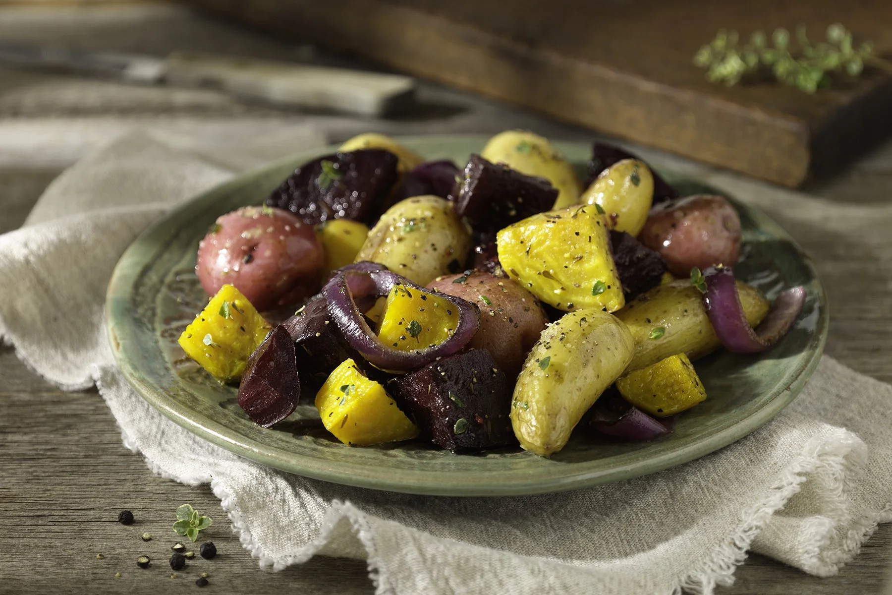 A plate of roasted new potatoes with beets and red onions, seasoned with herbs, on a rustic wooden table