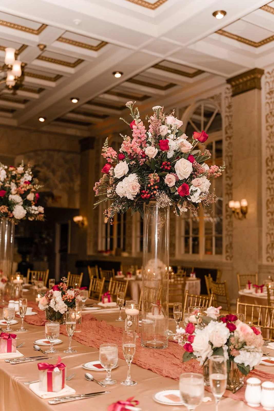 Elegant banquet hall decorated with large floral centerpieces, gold chairs, and well-set tables with glasses and silverware. Franklin Plaza Troy NY Wedding.