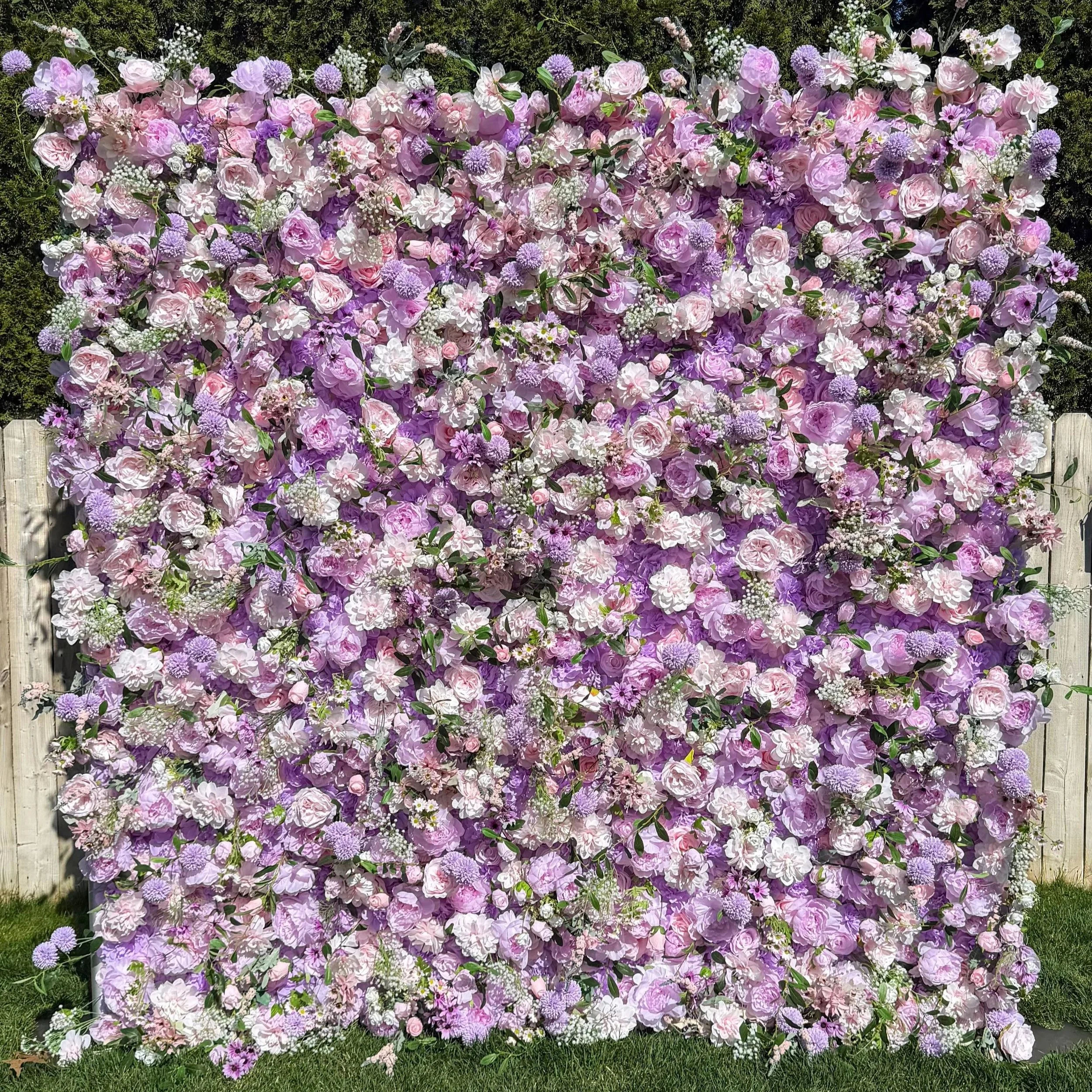 A large colorful floral wall with pink, purple, and white flowers and green leaves, set against a green hedge and grass.