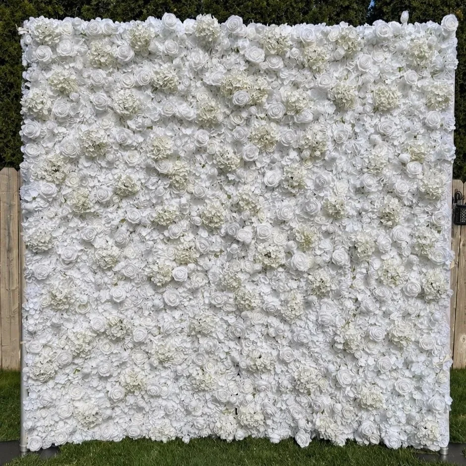 White floral backdrop made of numerous white roses and hydrangeas, set outdoors with a wooden fence and greenery in the background.