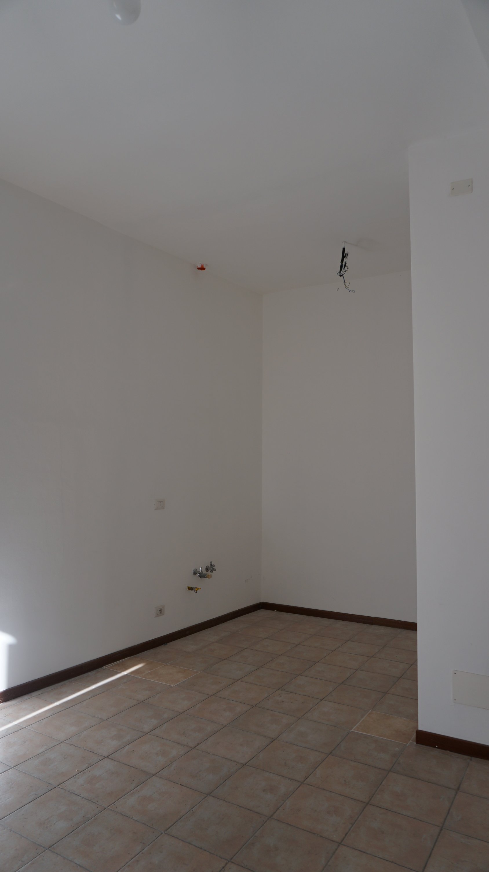 Stanza vuota in fase di ristrutturazione con pareti bianche, piastrelle beige e zona lavandino senza mobili.