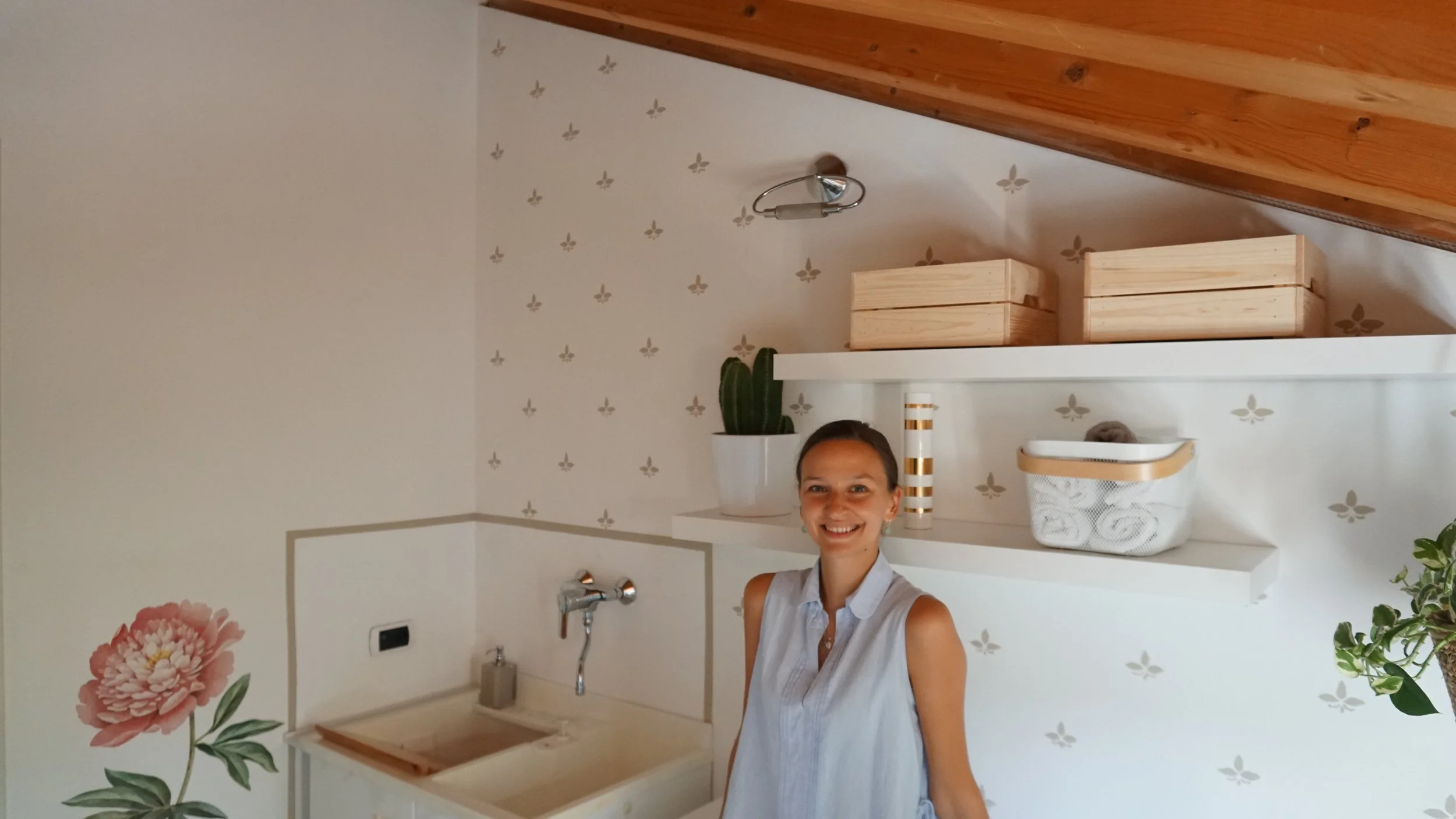 Donna sorridente in una cucina moderna con scaffali bianchi, piante e decorazioni floreali sulle pareti