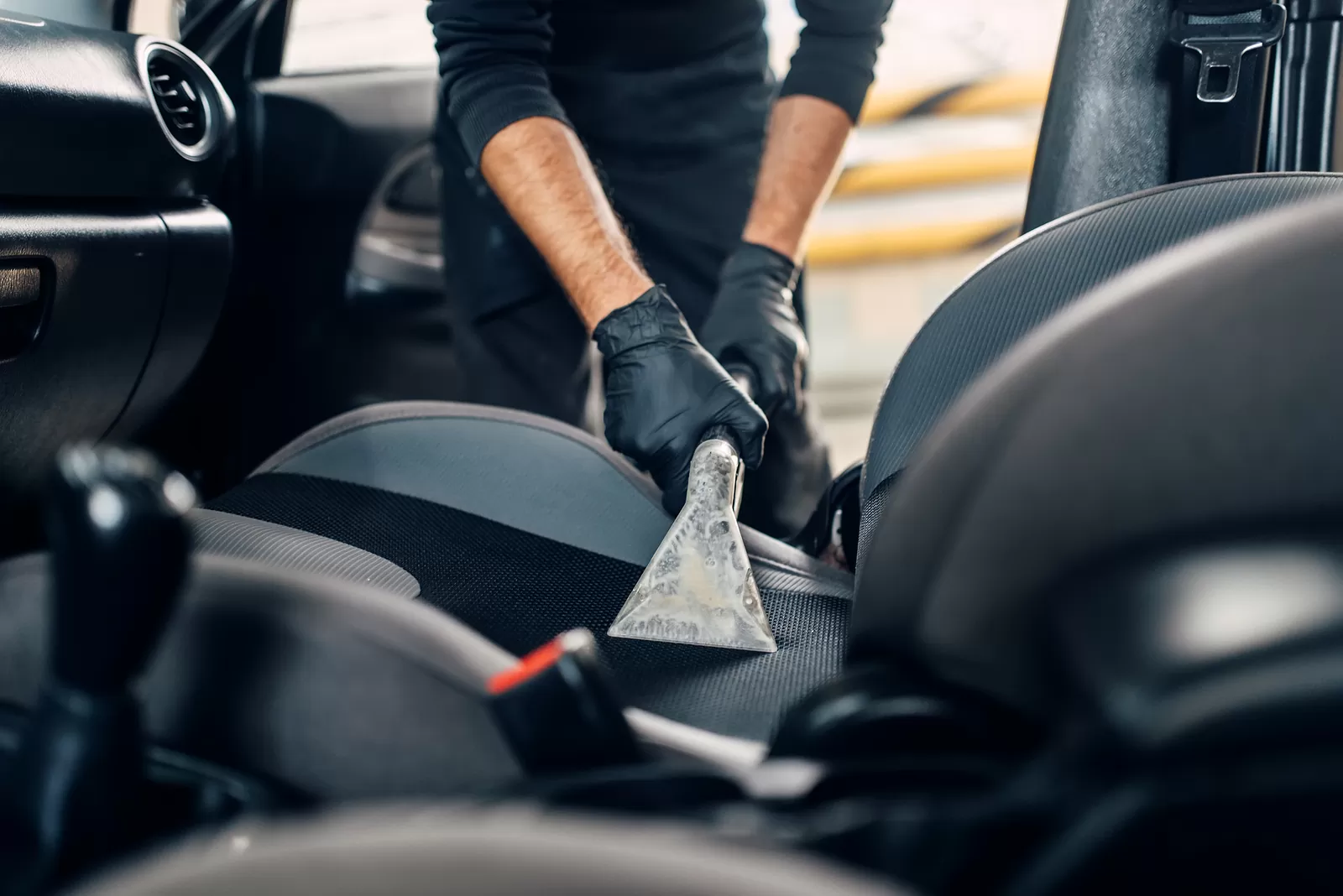 Person wearing black gloves cleaning the interior of a car with a handheld scraper.