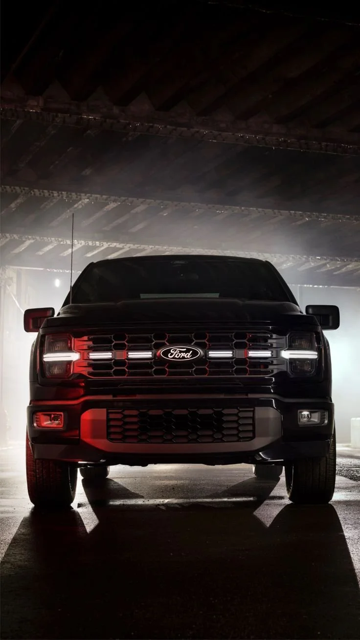 Front view of a black Ford pickup truck in a dimly lit garage with bright backlighting.