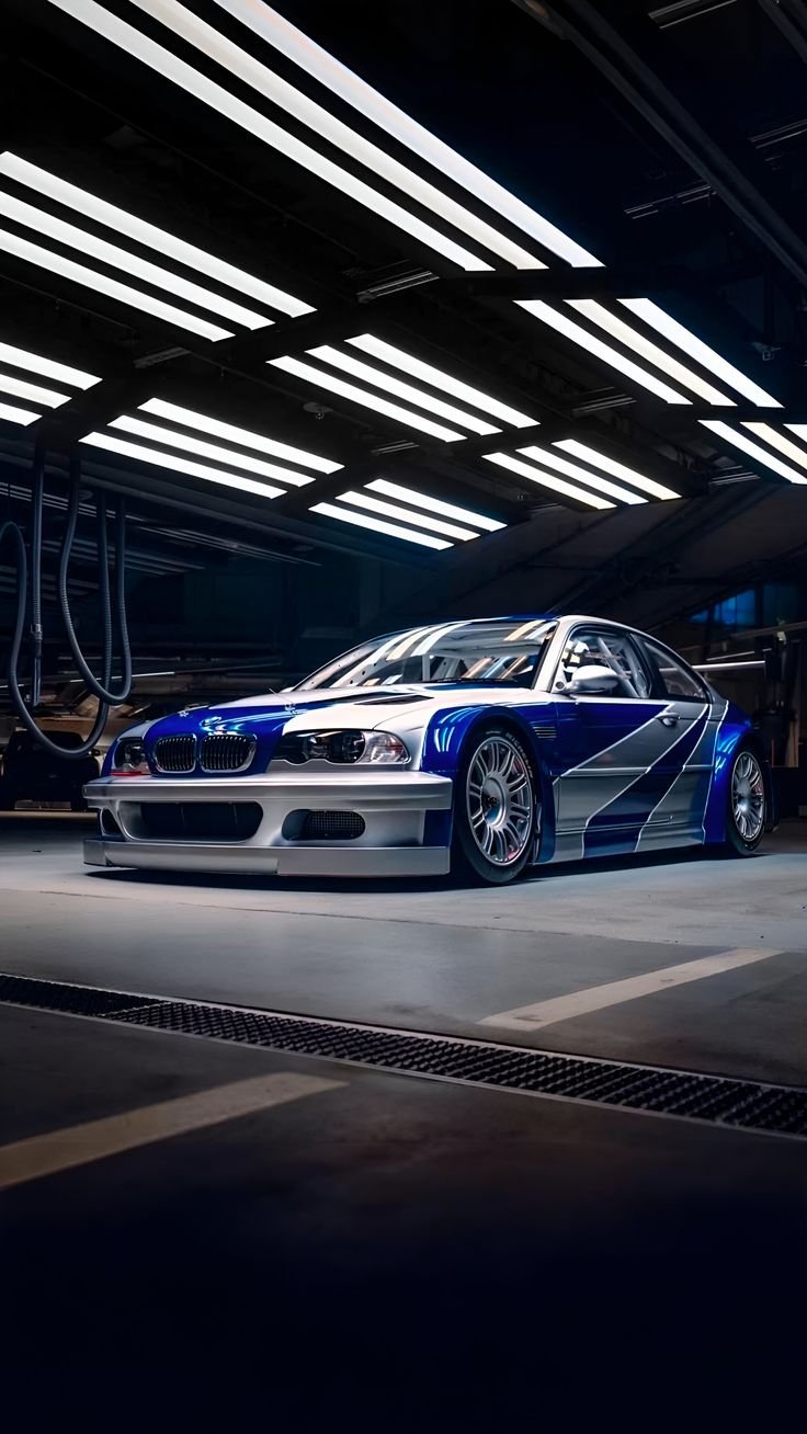 A race car in a garage with bright overhead lights, painted blue and silver with aerodynamic features.