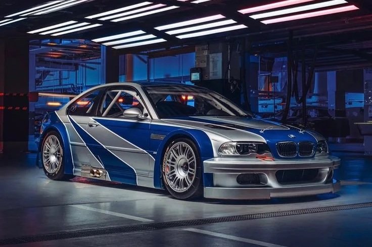 A silver and blue race car with sponsorship graphics parked inside a garage with bright overhead lighting.