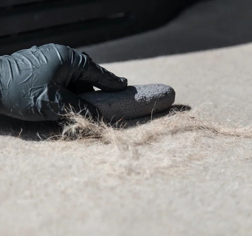 Person wearing black gloves using a stone to smooth fabric fibers on light-colored surface.