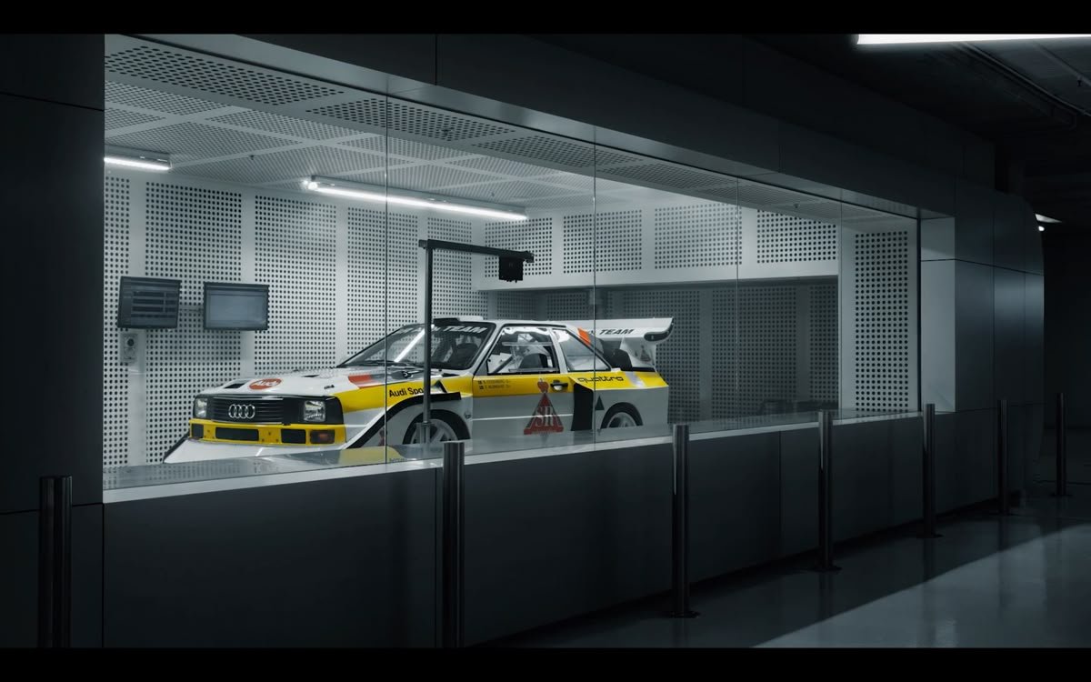 A vintage Audi rally car displayed inside a glass case at a museum or exhibit, with a white and yellow color scheme and racing decals.