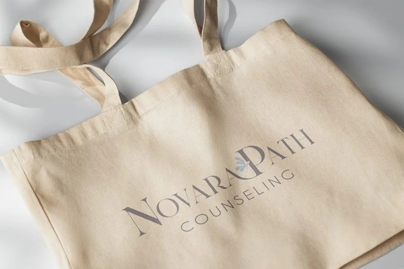 A beige cloth tote bag with the words "NovarPath Counseling" printed on it, featuring a small logo with a blue leaf.