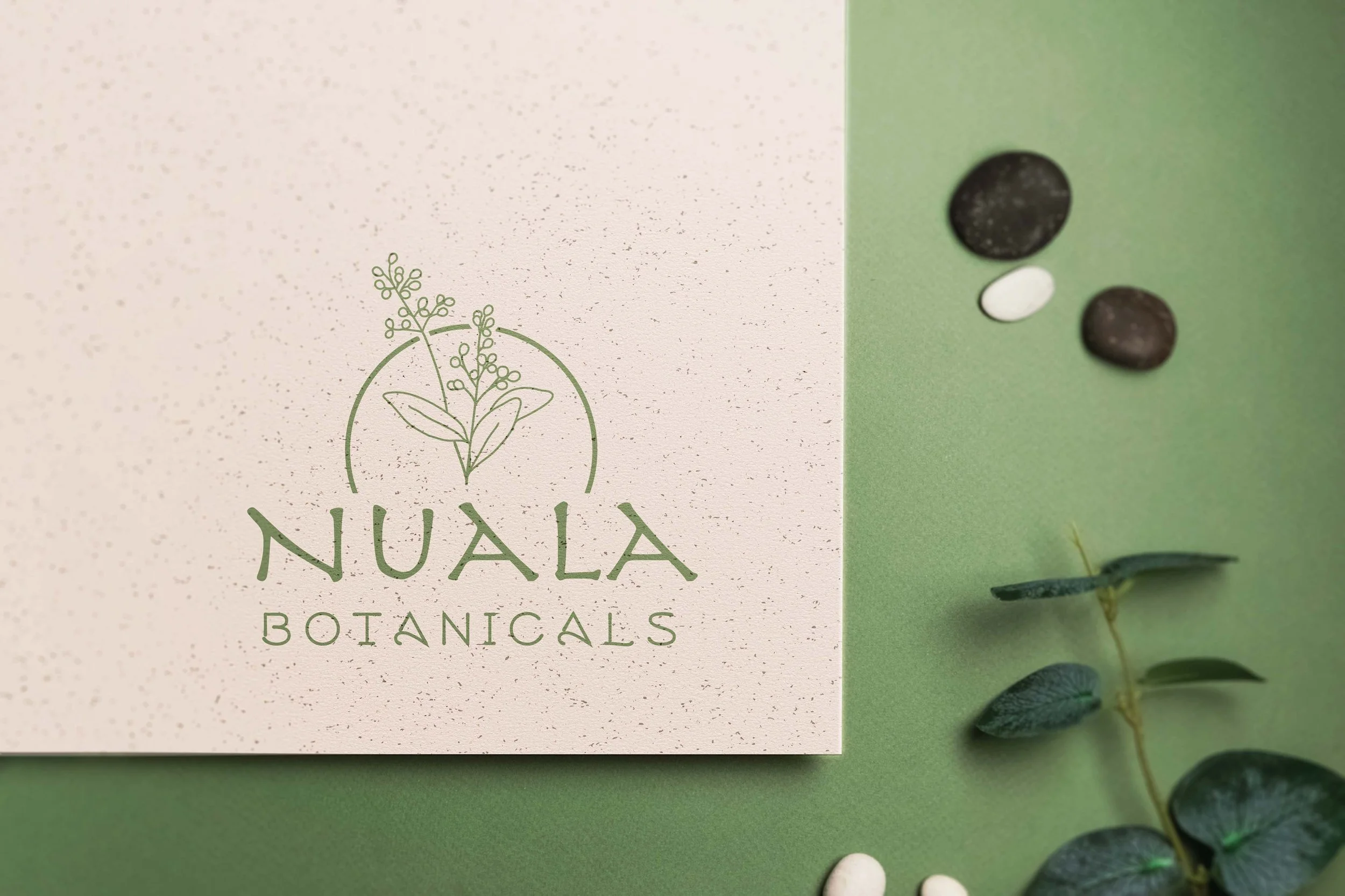 Nuala Botanicals logo on a textured white card with green plant illustrations, placed on a green background with assorted pills and a small green plant beside it.