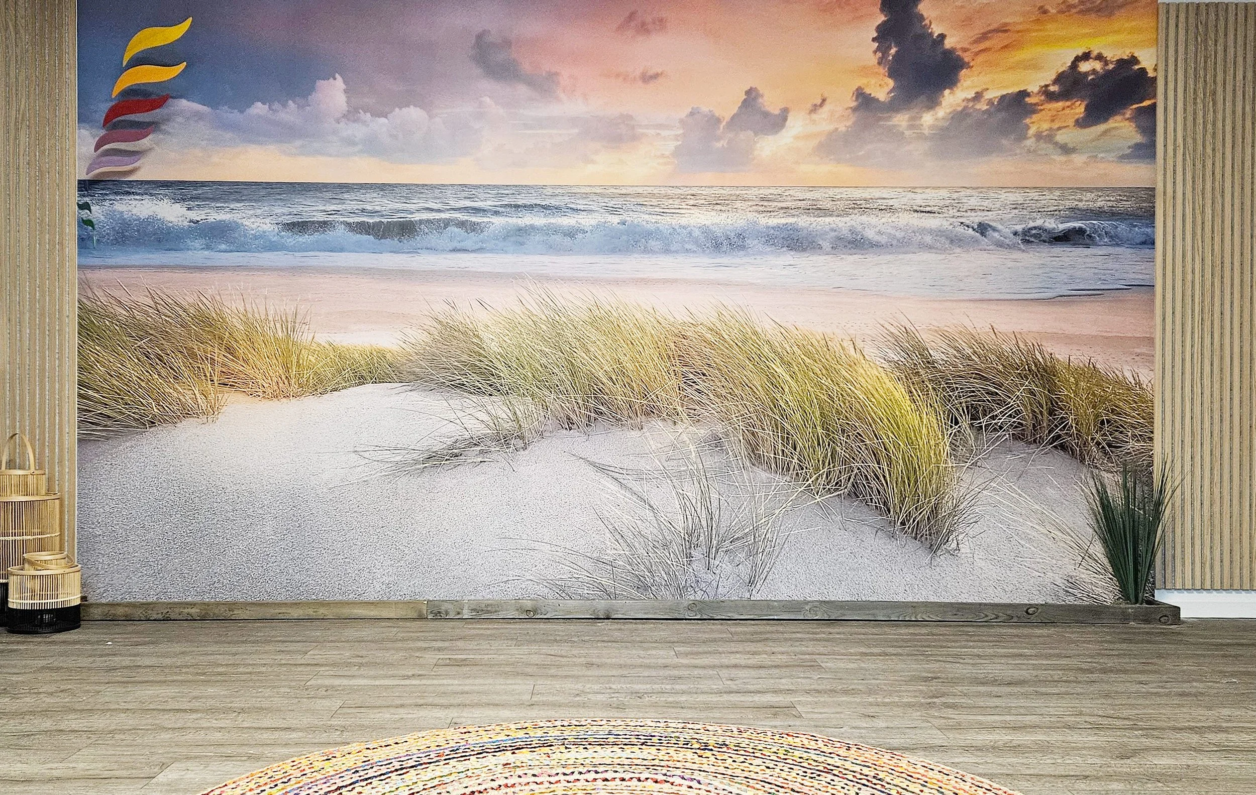 Wanddekoration mit Strandmotiv, das Sanddünen, Gras und ein Meer mit Wellen bei Sonnenuntergang zeigt.